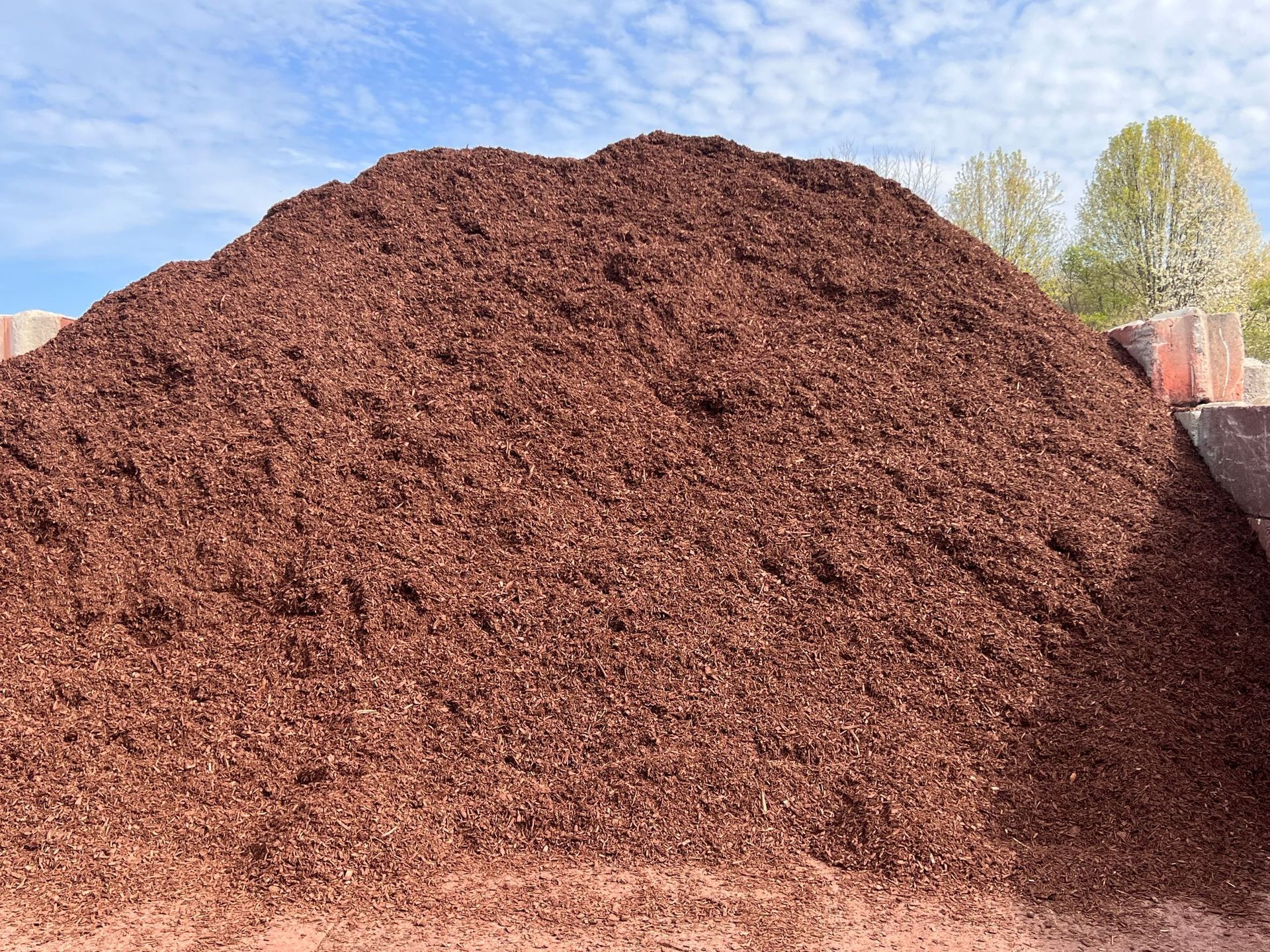 Pile of dark red mulch under a partly cloudy sky.