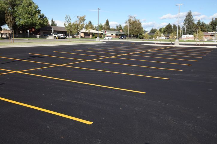 A freshly paved, empty parking lot with bright yellow painted lines under a clear blue sky.