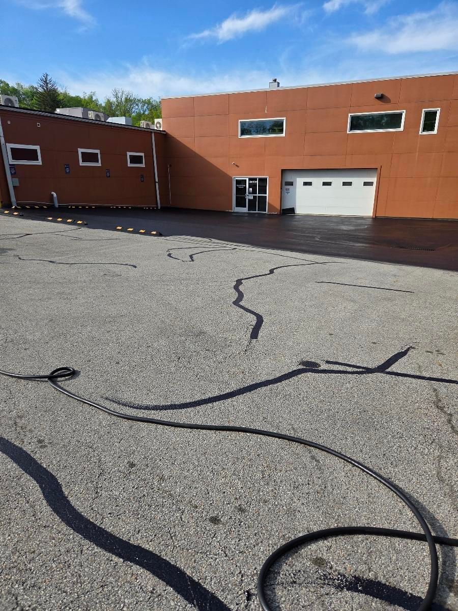 A commercial building with an orange facade and white garage doors above a gravel lot with black crack-sealant lines.
