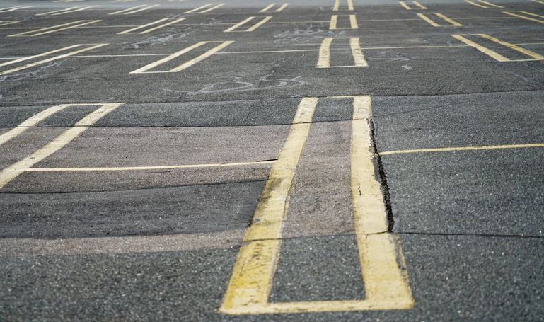 A close-up of a paved parking lot with faded, double-lined yellow markings indicating parking spaces.