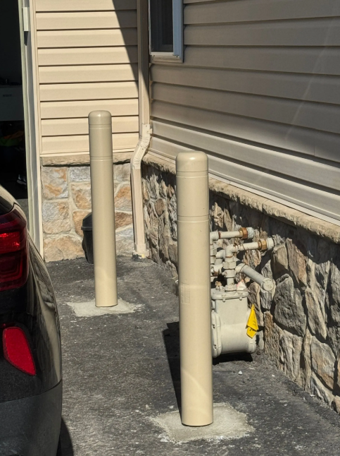 Two beige bollards on a driveway beside a house and parked car