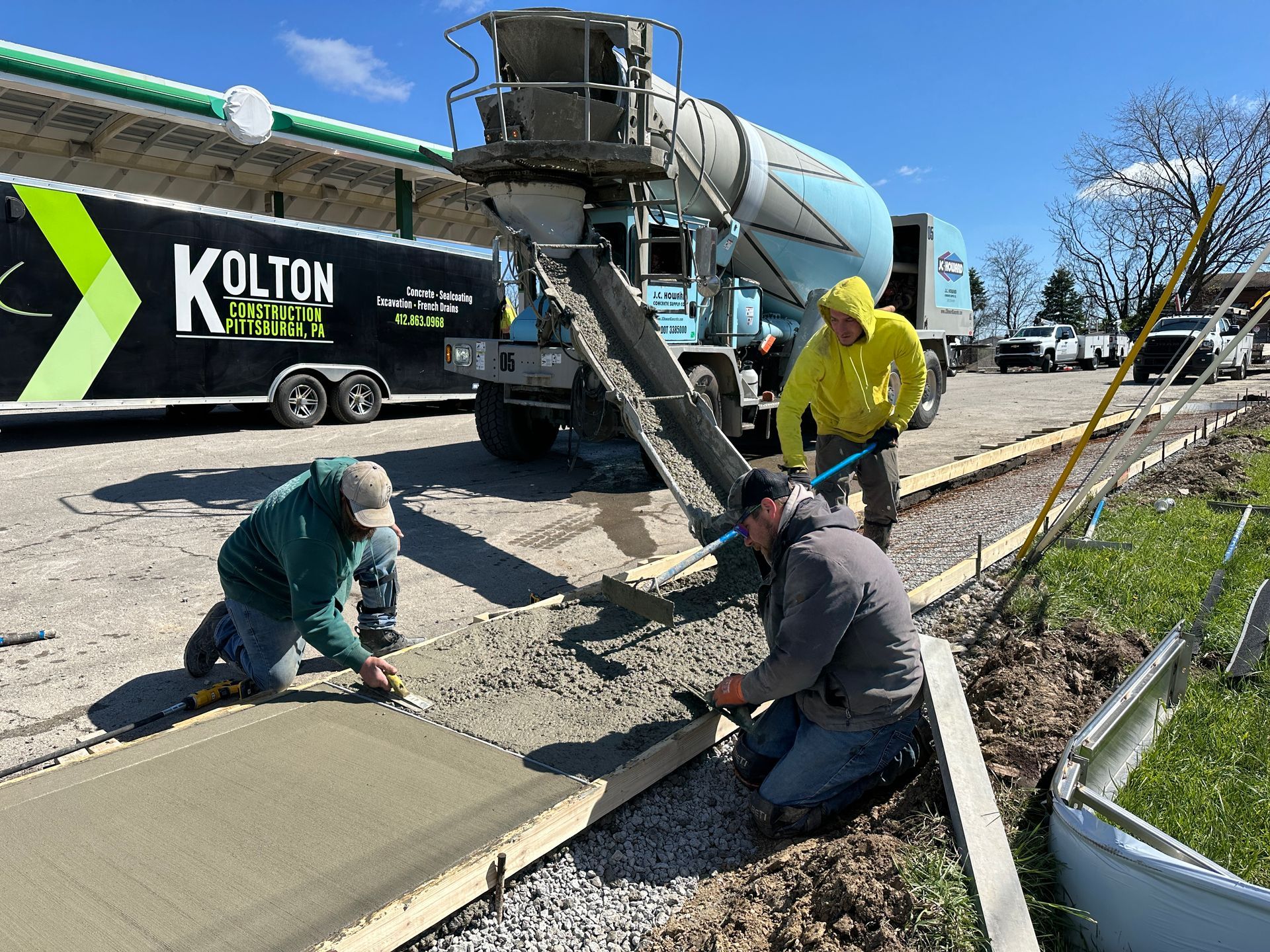 Road crew pouring concrete from a mixer truck onto a sidewalk in bright daylight