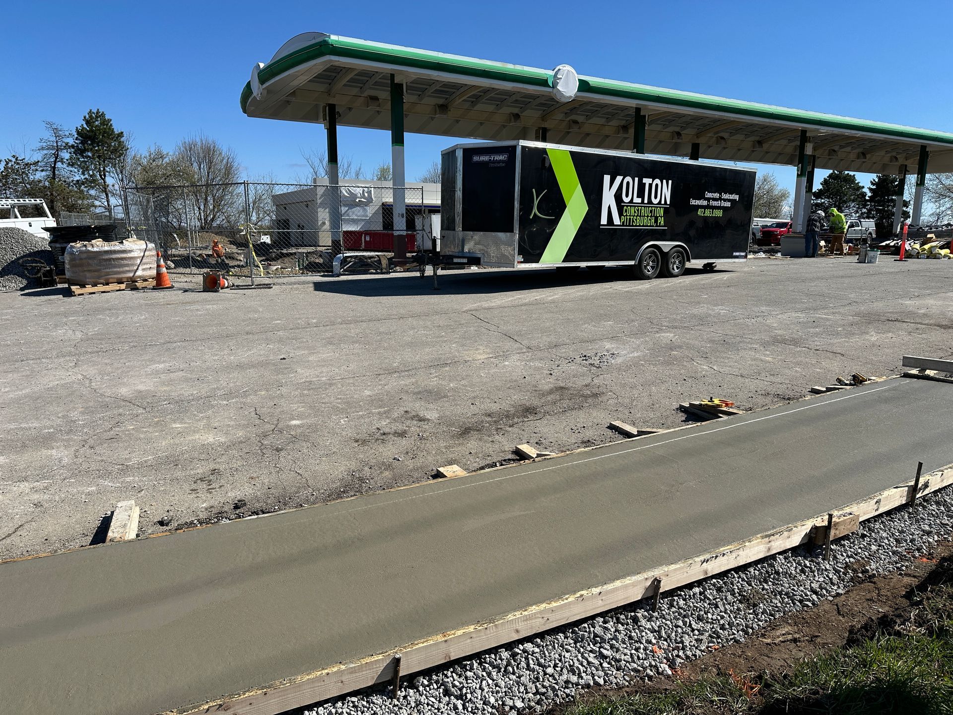 Black trailer parked under a green canopy at a gravel lot with construction debris nearby