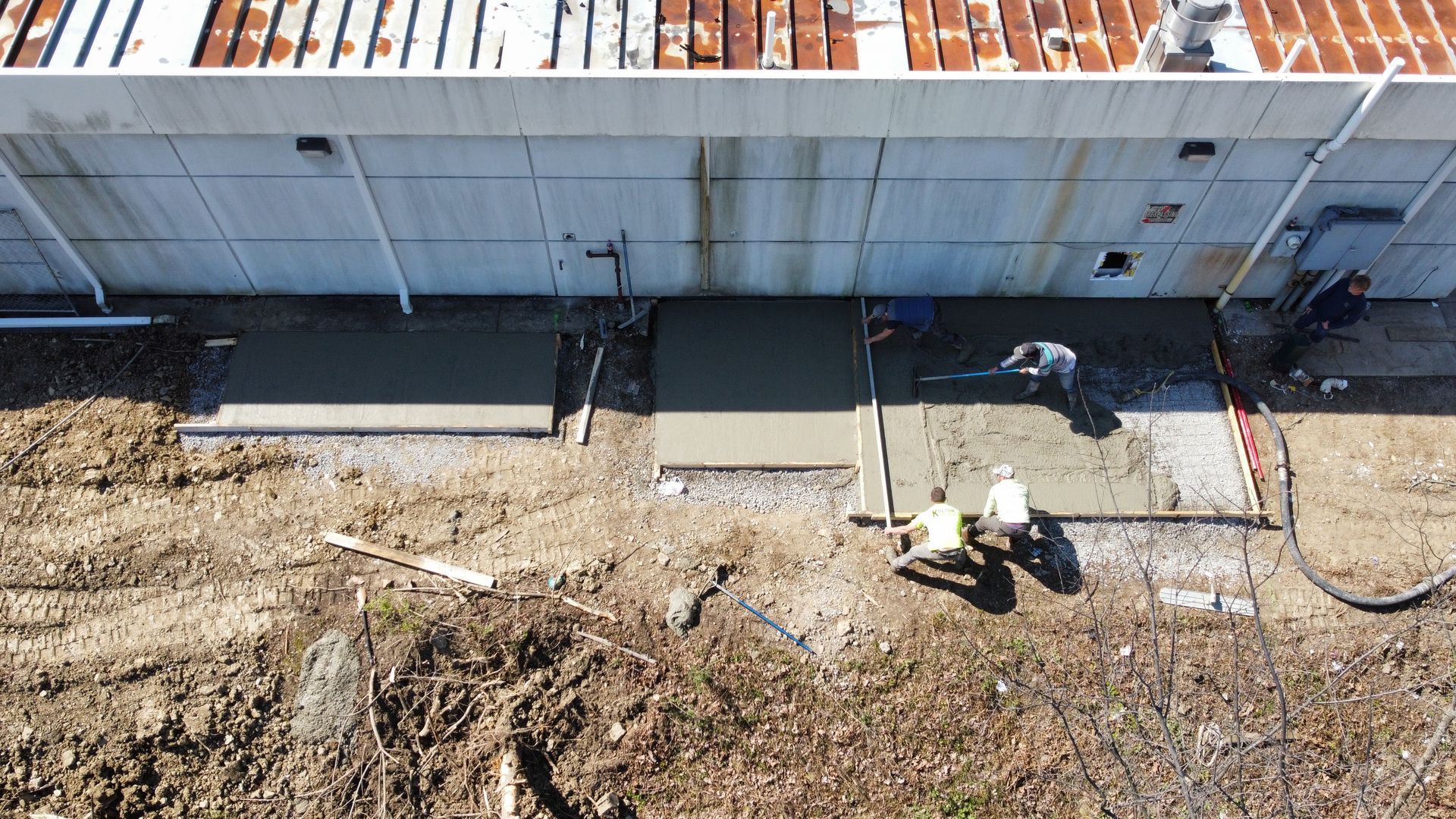 Two workers pouring concrete along the base of a building wall outdoors