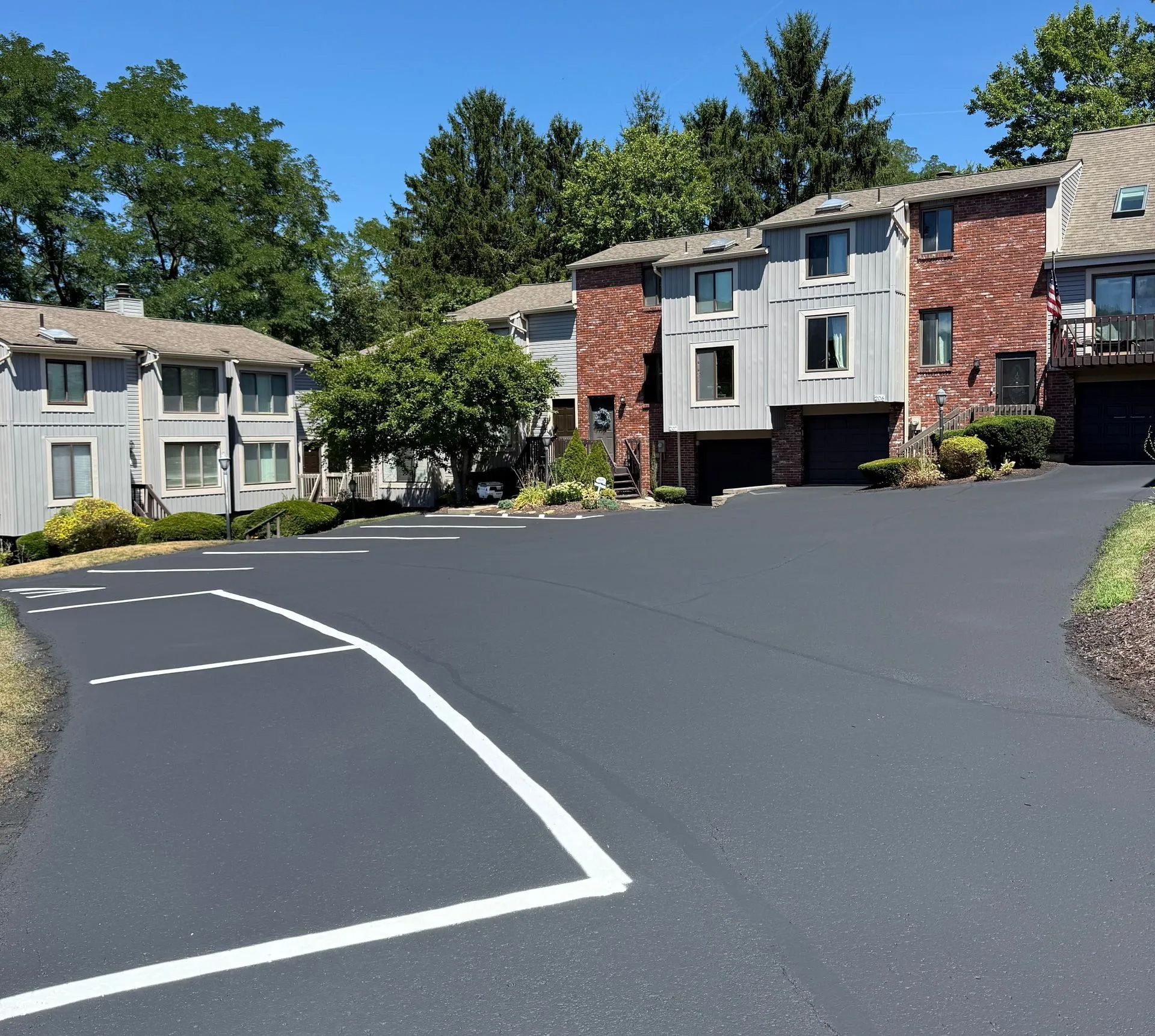 A newly paved asphalt parking lot with white painted lines in front of a residential apartment complex with brick facades.