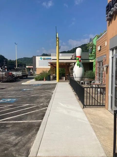 A sidewalk leads past a large bowling pin statue toward a commercial building with mountains in the background.