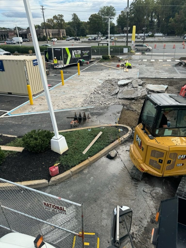 Construction site with excavator, gravel piles, fenced area, and paved roadway