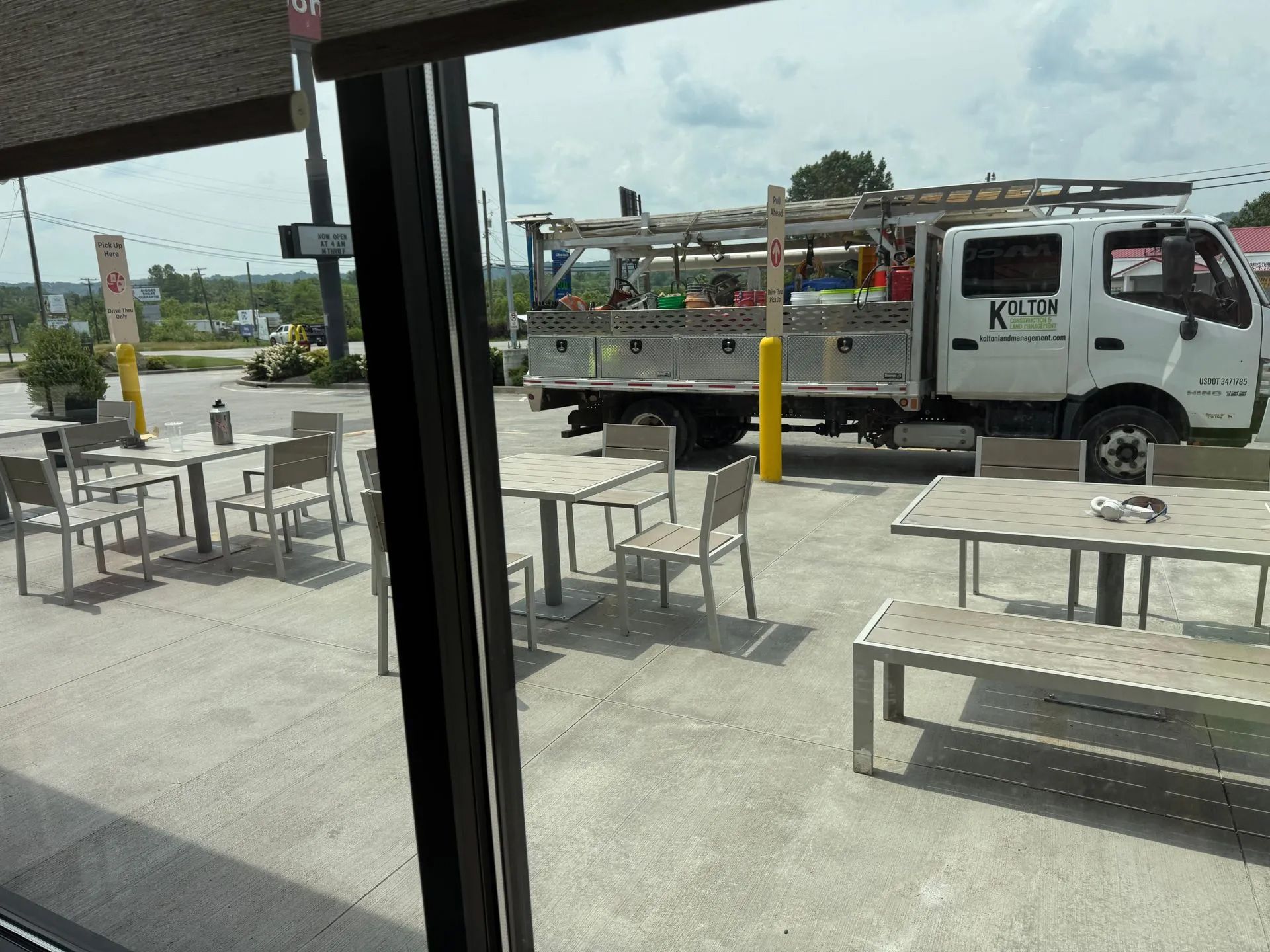 An outdoor patio with metal tables and chairs, with a white utility truck parked in the background under a cloudy sky.