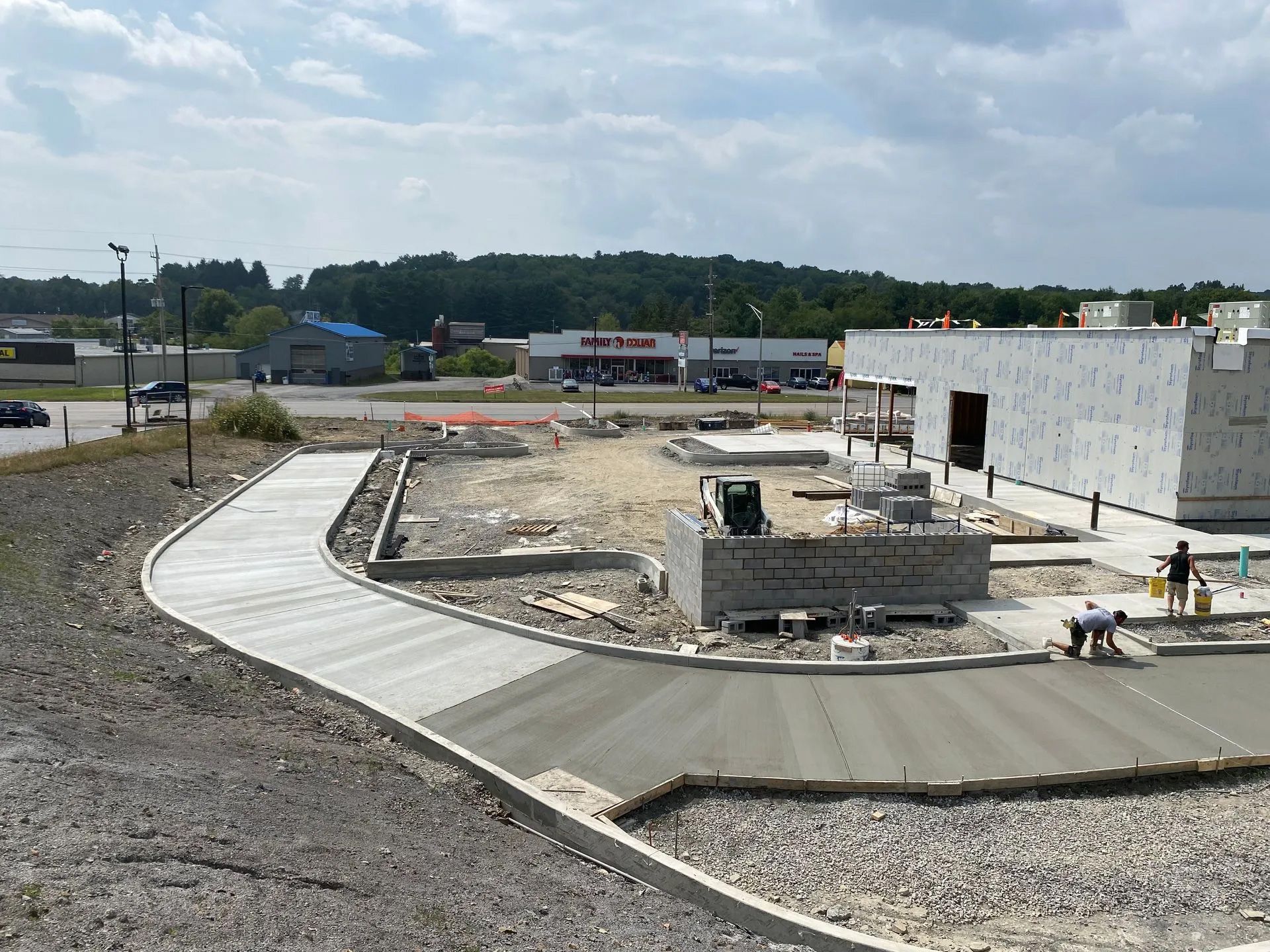 Construction site with curved concrete walkway, gravel, and a white building under construction