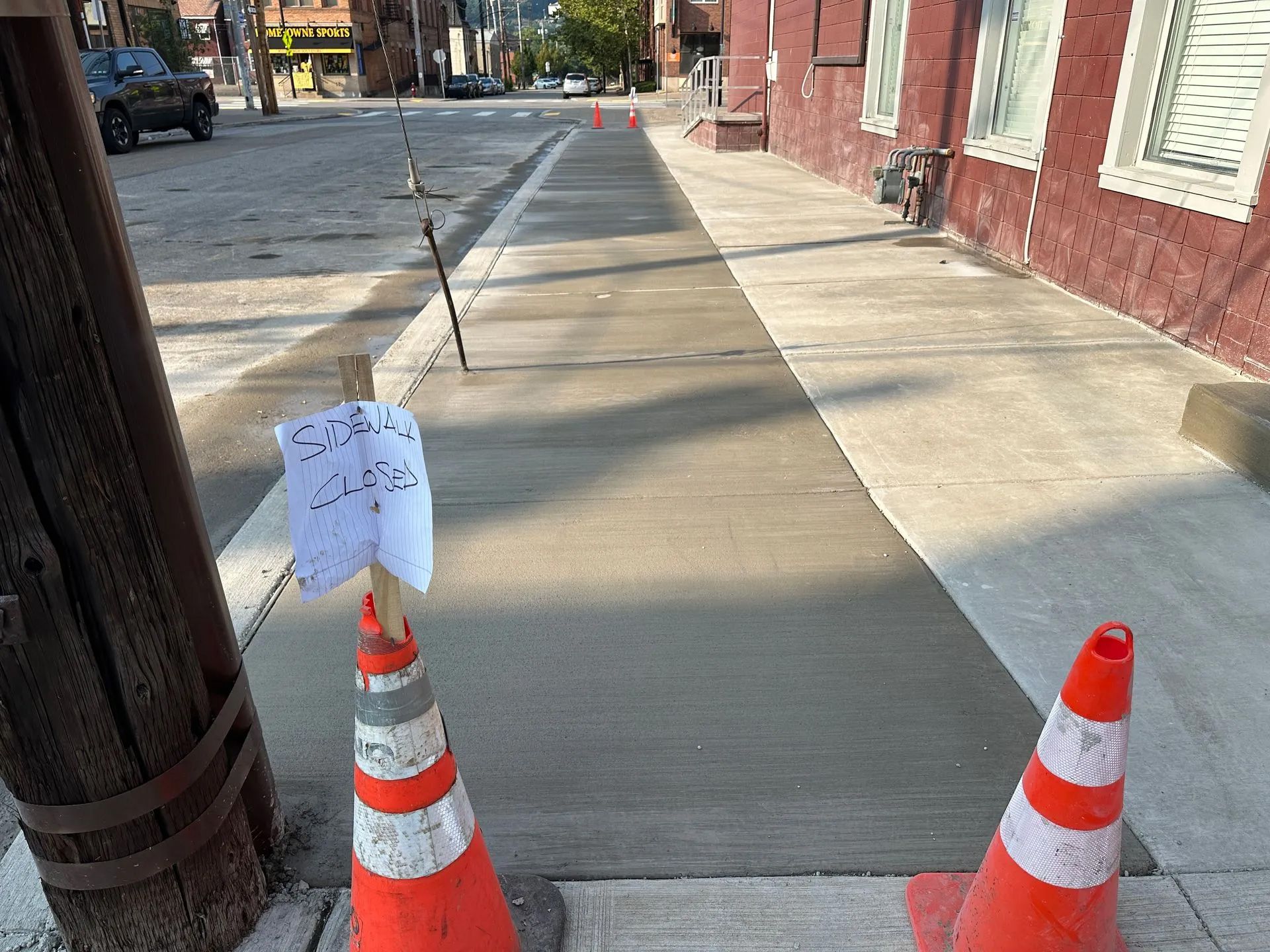 Freshly poured sidewalk concrete blocked off with orange traffic cones and a sign warning to keep off.