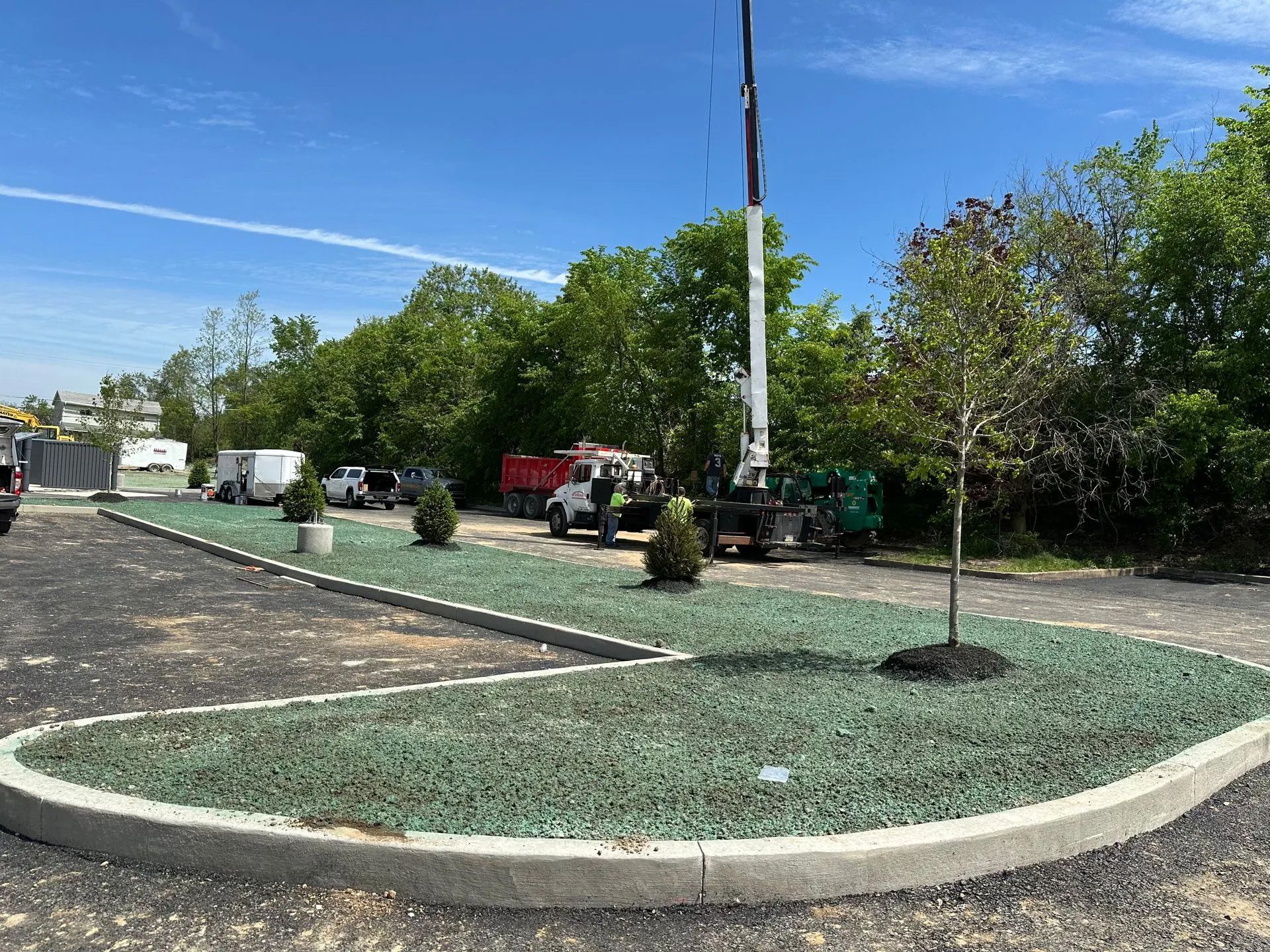 A construction scene with a crane, vehicles, and a newly landscaped parking island with green stone mulch and young trees.