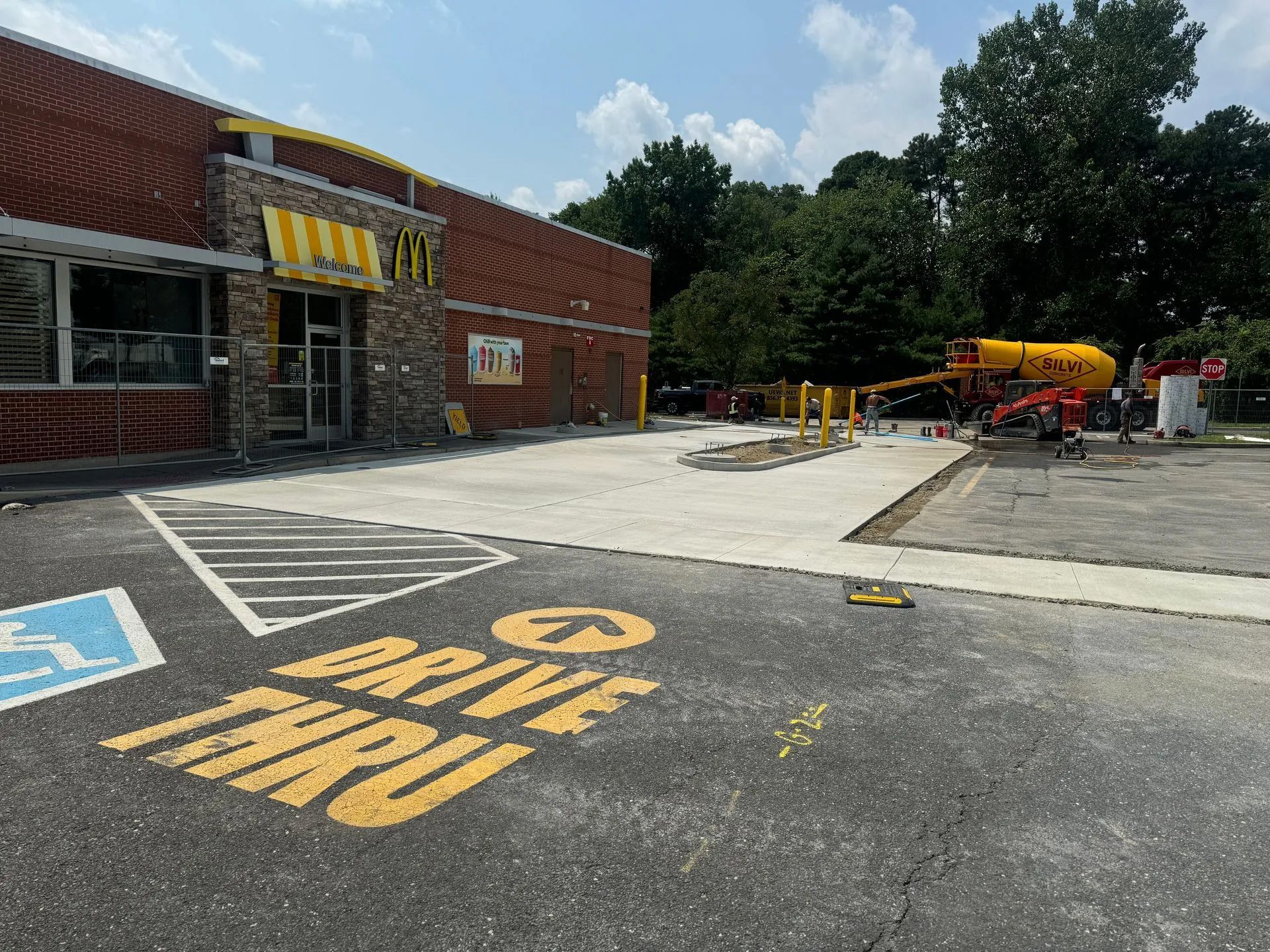A McDonald's restaurant undergoing construction with new concrete pavement, drive-thru markings, and a yellow mixer truck.