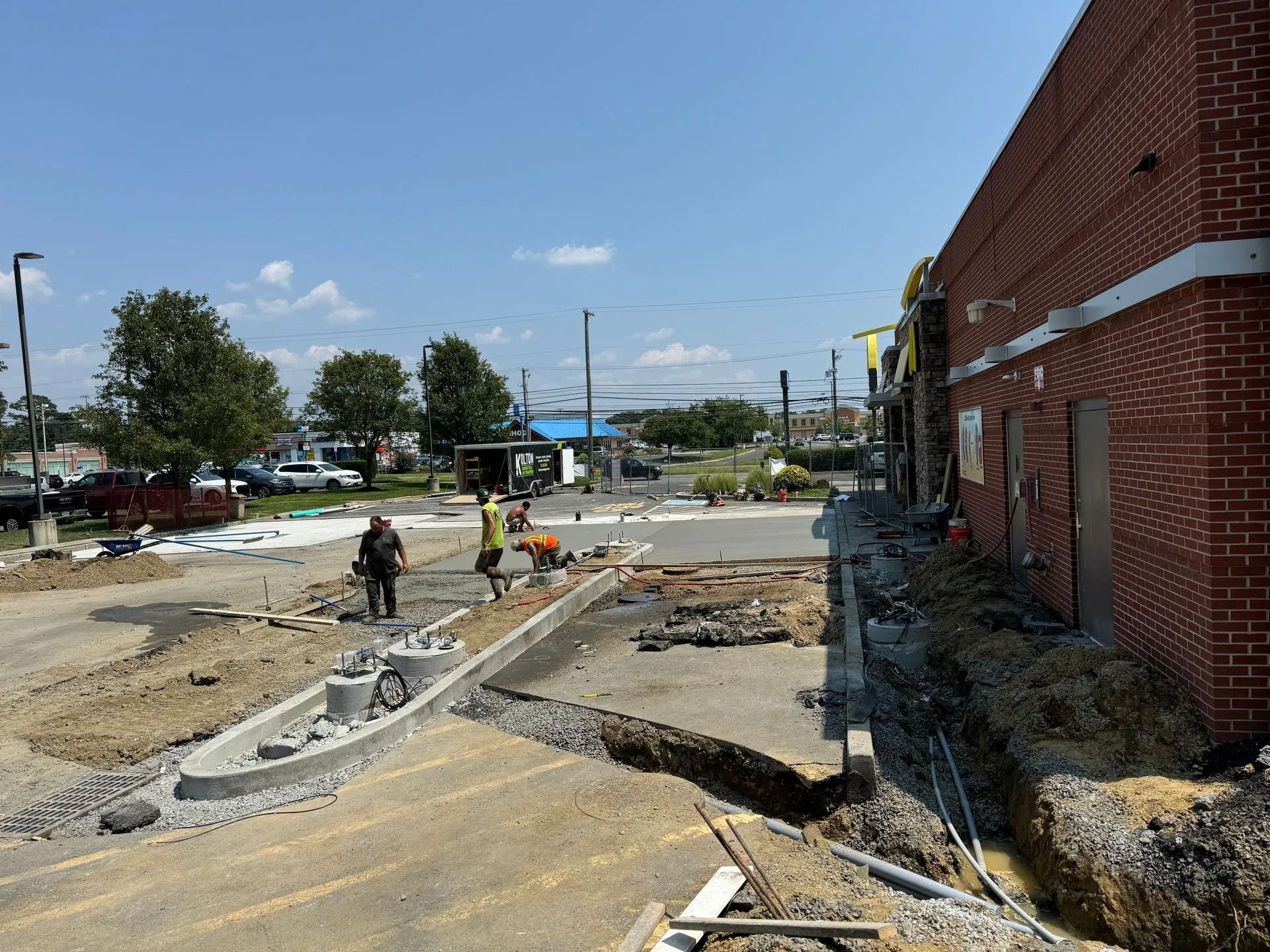 Construction workers installing a concrete curb in front of a brick commercial building on a sunny day.
