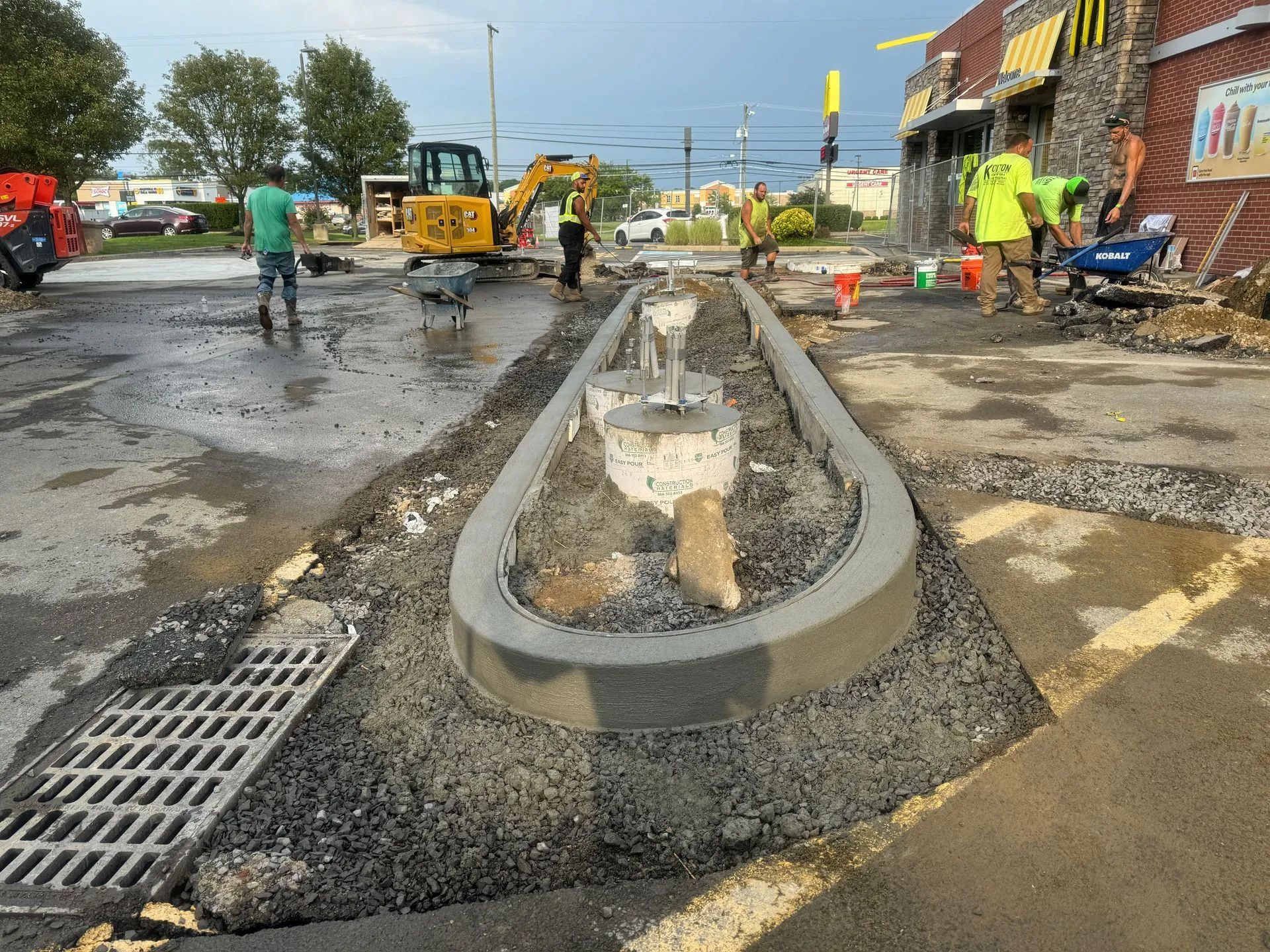 Construction workers improve a McDonald's parking lot with a new concrete curb, gravel, and an open storm drain.