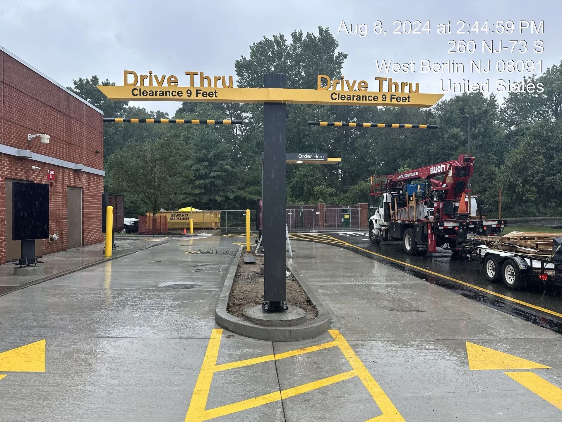 A rainy drive-thru entrance with two lanes separated by a yellow-marked concrete island and a large overhead sign.