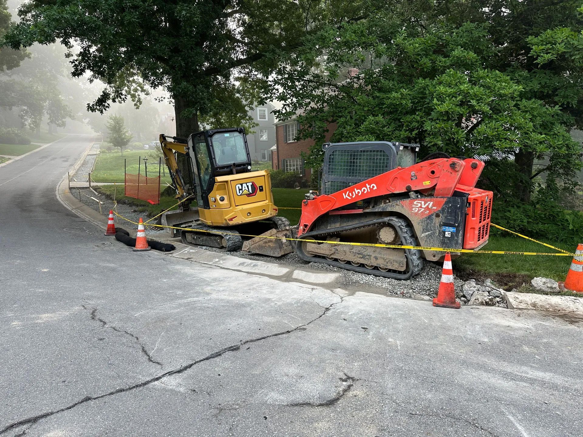 Yellow skid steer and red tow truck on a roadside construction area with cones and caution tape.