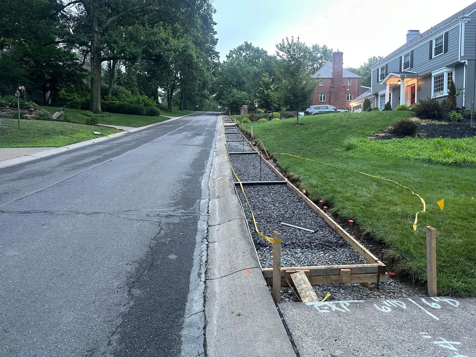 A residential street showing a roadside construction project where a wooden form is prepared for a new concrete curb.