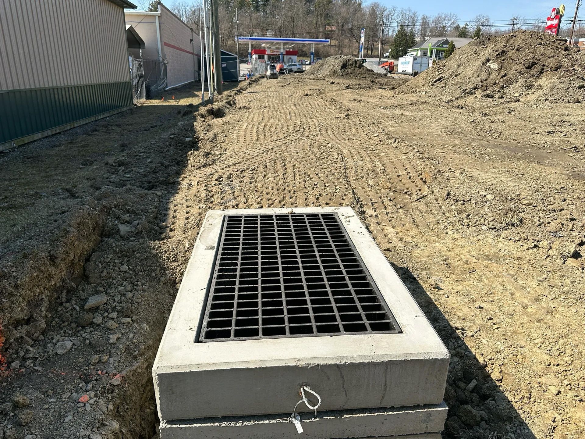 Concrete storm drain grate in a dirt construction area beside a road