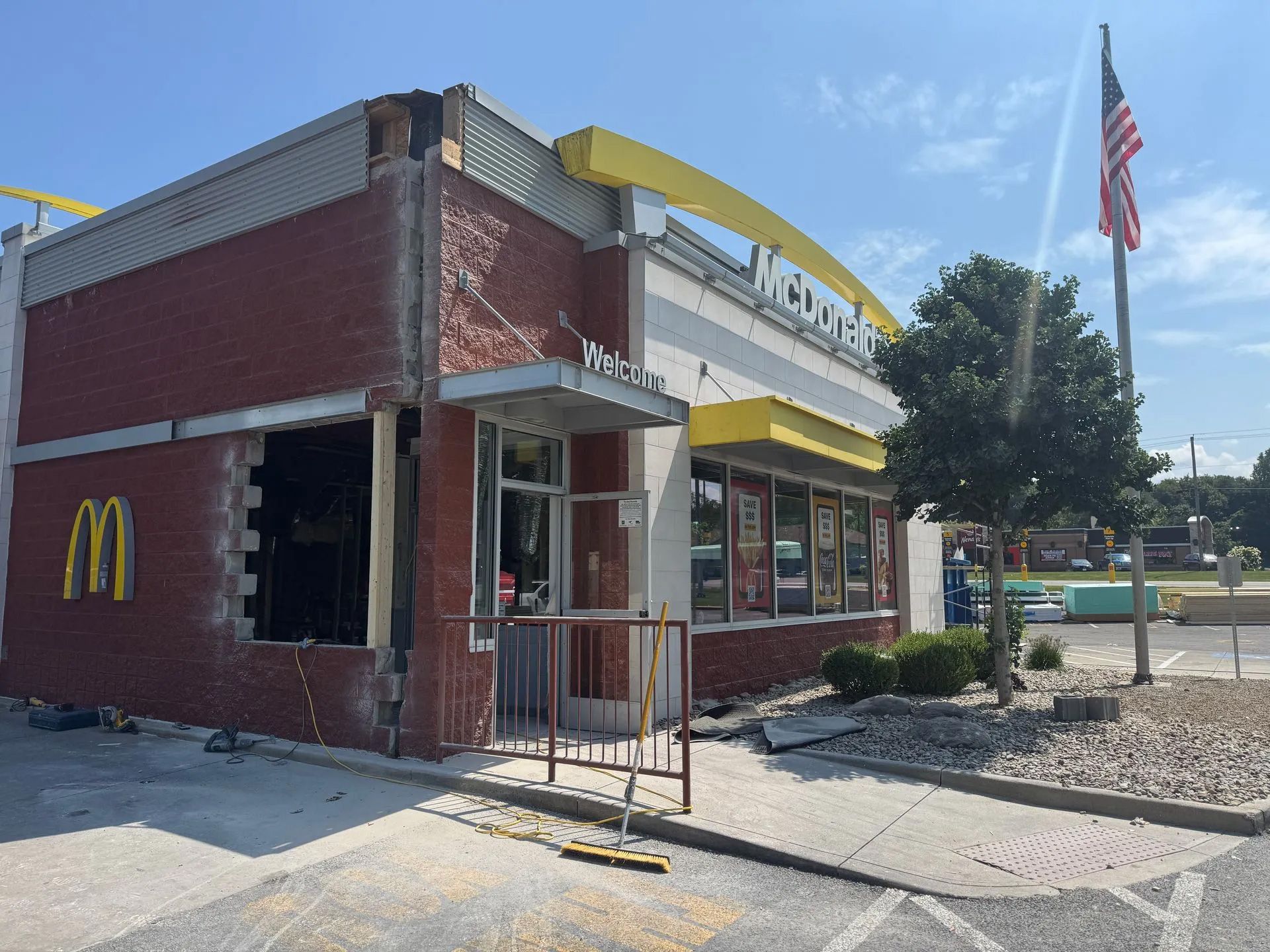 A damaged McDonald's restaurant with a collapsed brick wall corner and exposed interior framing under a blue sky.