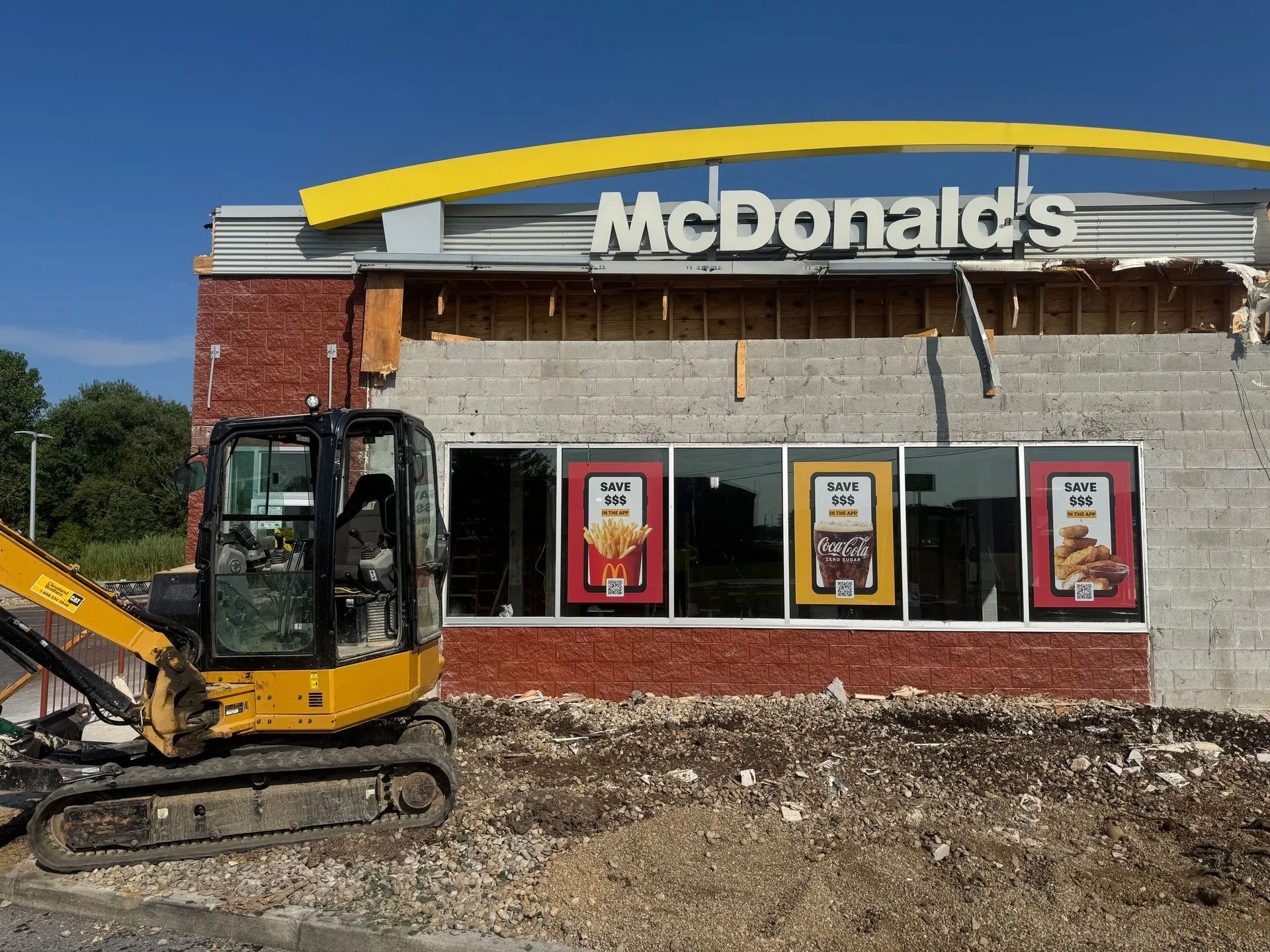 McDonald's storefront under demolition with an excavator in front, yellow trim visible on roof.