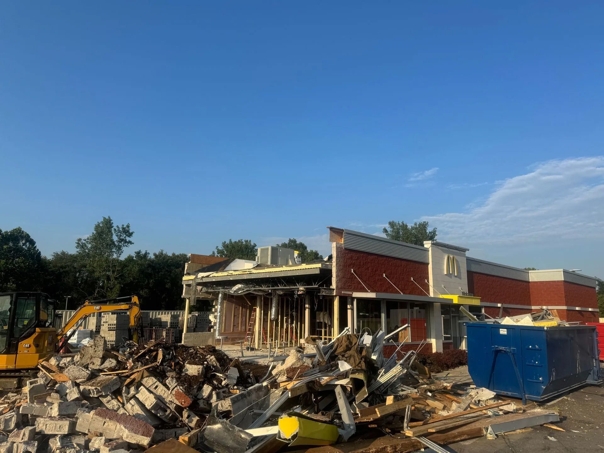 Demolition site with rubble, excavator, and a partially torn-down building under a clear blue sky