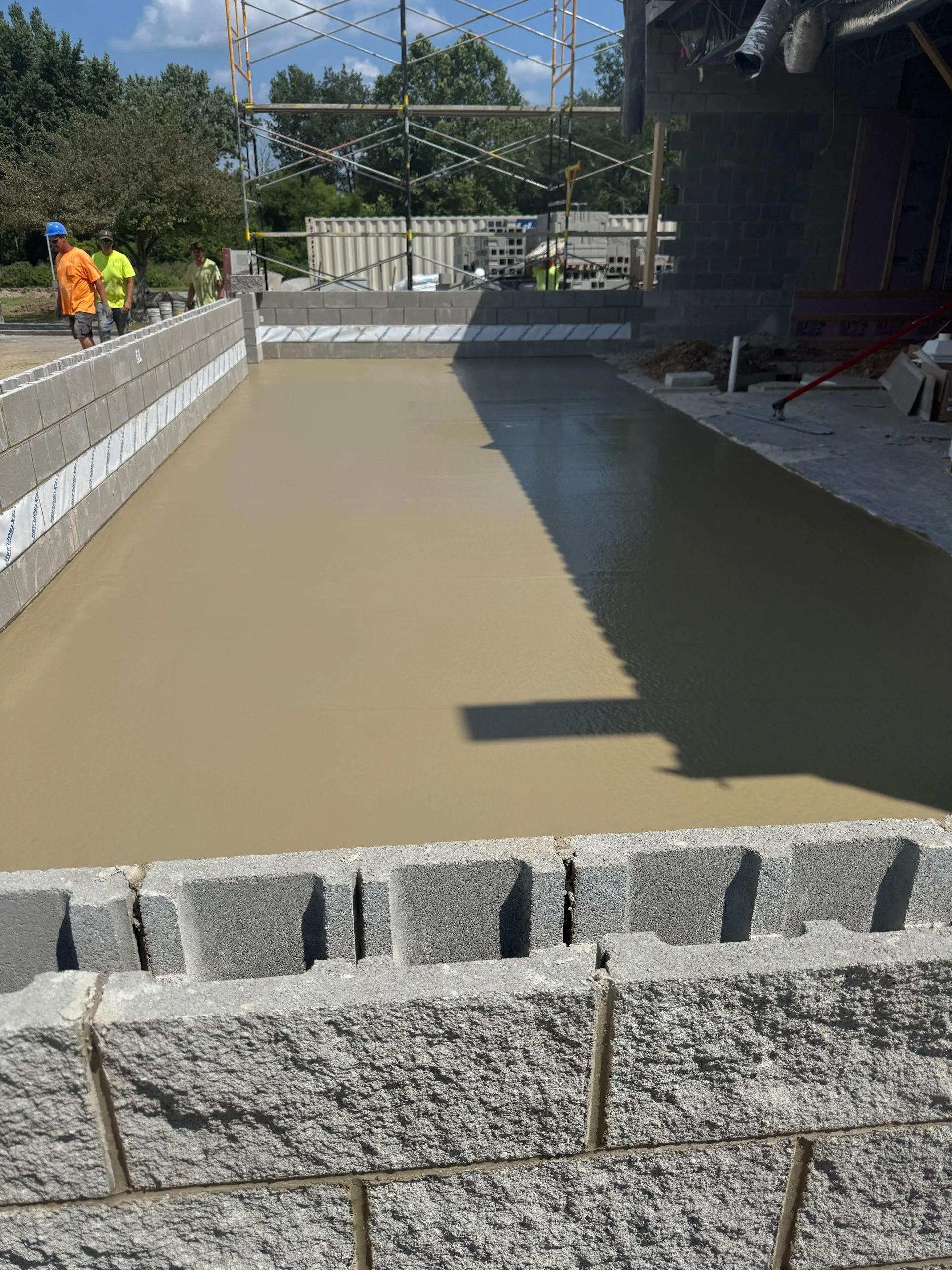 Freshly poured concrete foundation within a rectangular perimeter of grey concrete blocks at a construction site.
