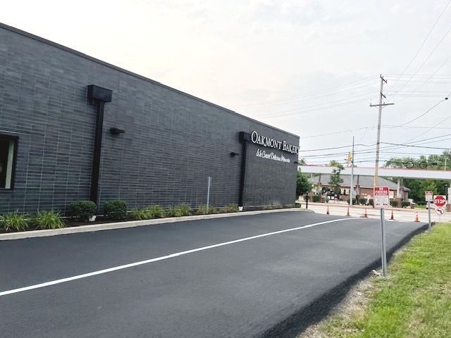 An exterior view of the Oakmont Bakery building with a dark brick facade next to a newly paved asphalt parking lot.