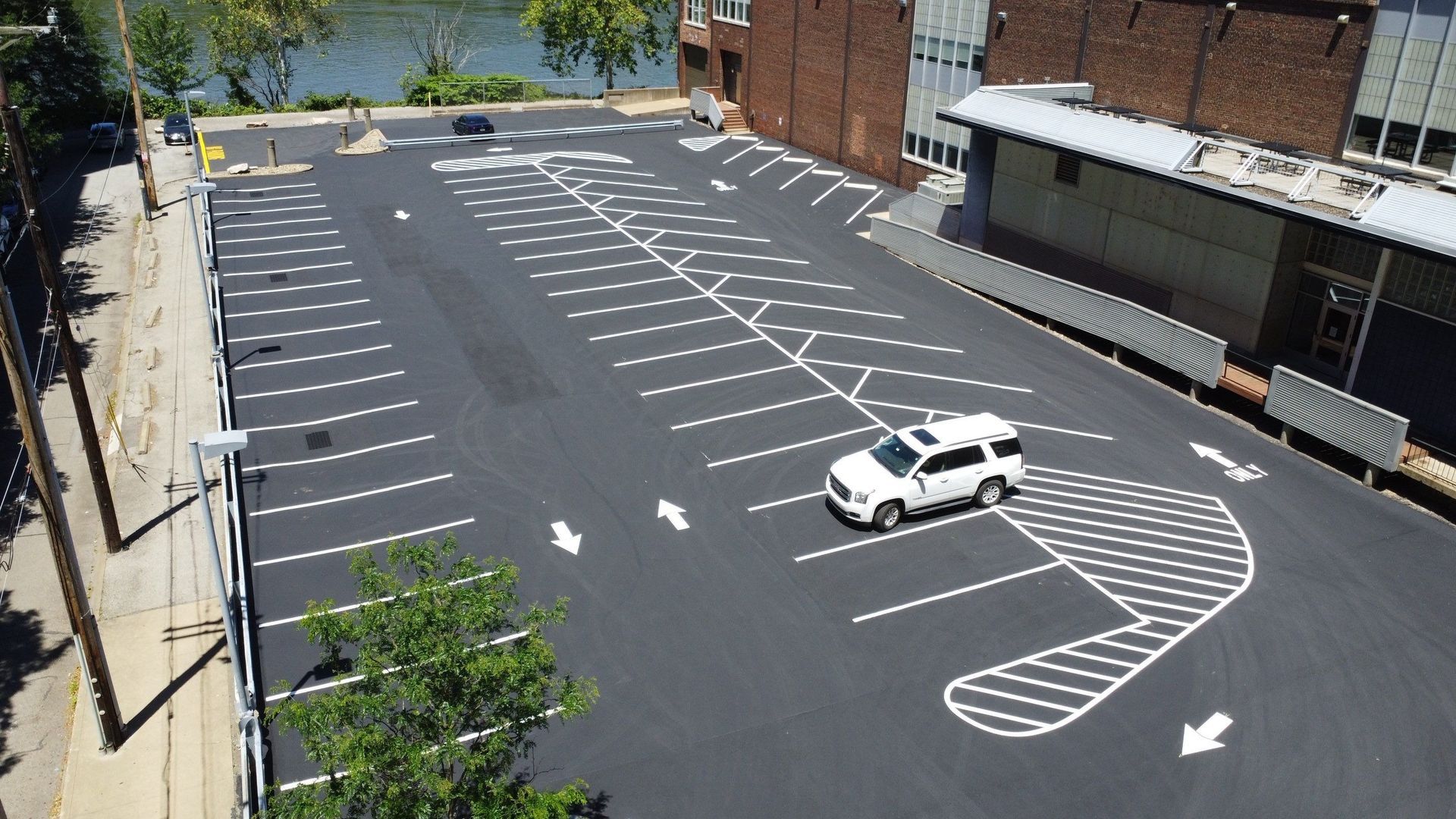 Empty parking lot with marked spaces and a white SUV near a brick building.