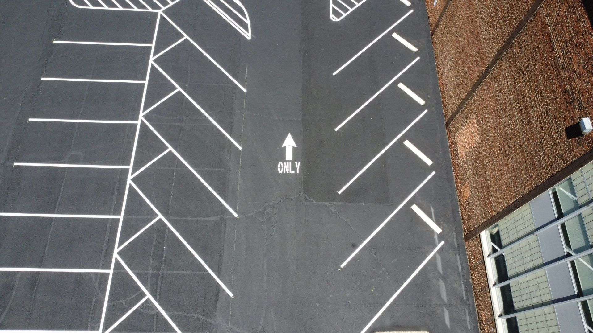 Empty parking lot with white diagonal parking lines and an arrow on dark pavement beside a brick wall.