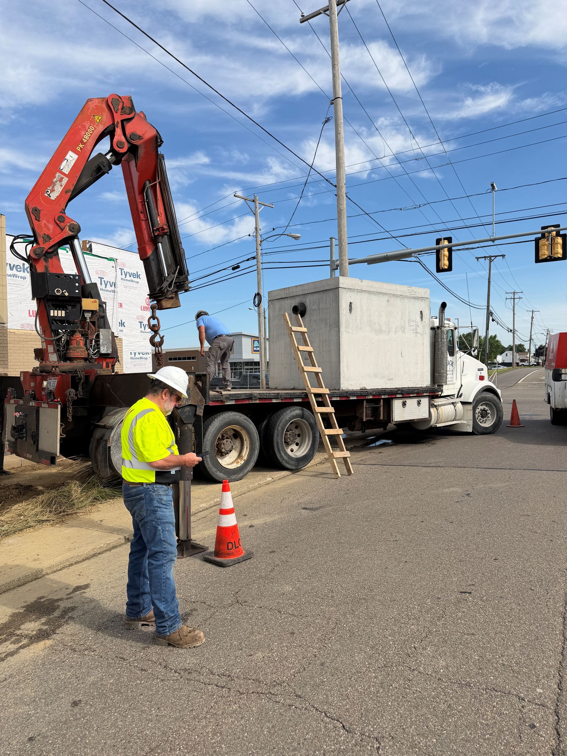 Worker in a neon vest near a truck-mounted crane at a road intersection.