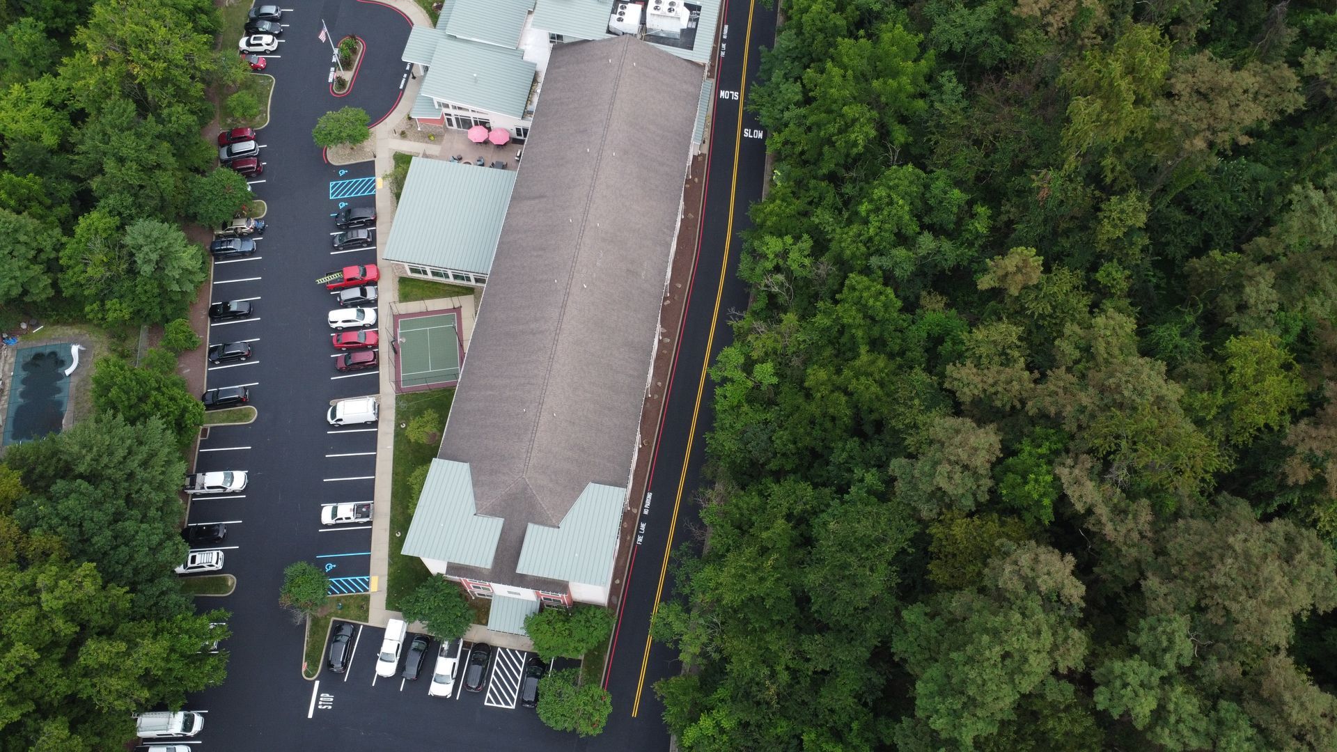 Aerial view of a long building beside a parking lot, bordered by dense green trees.