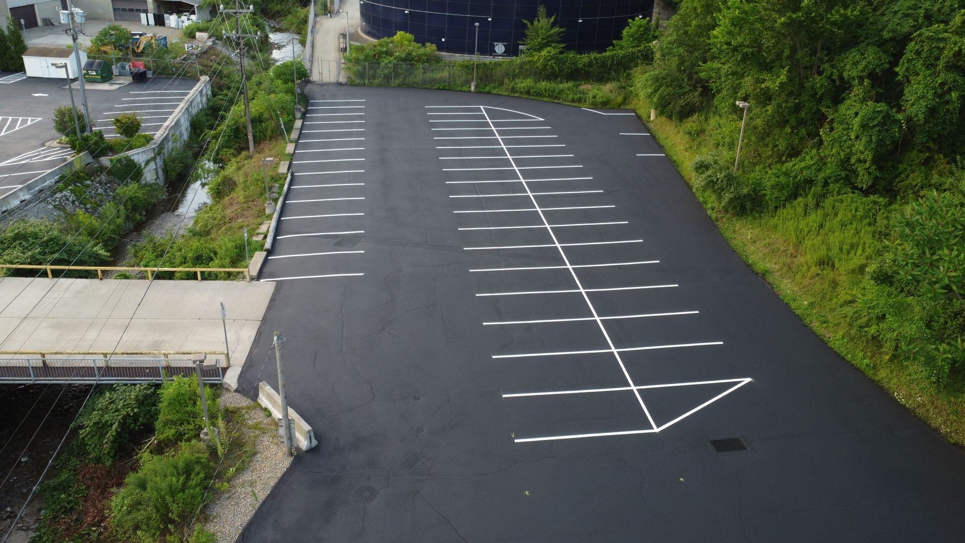 Empty parking lot with white stall lines beside a sidewalk and trees