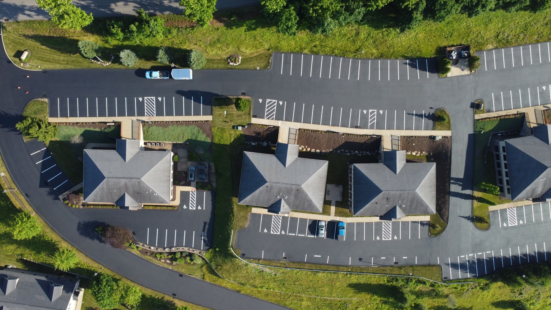 Aerial view of apartment buildings with parking lots and parked cars along a curved road.