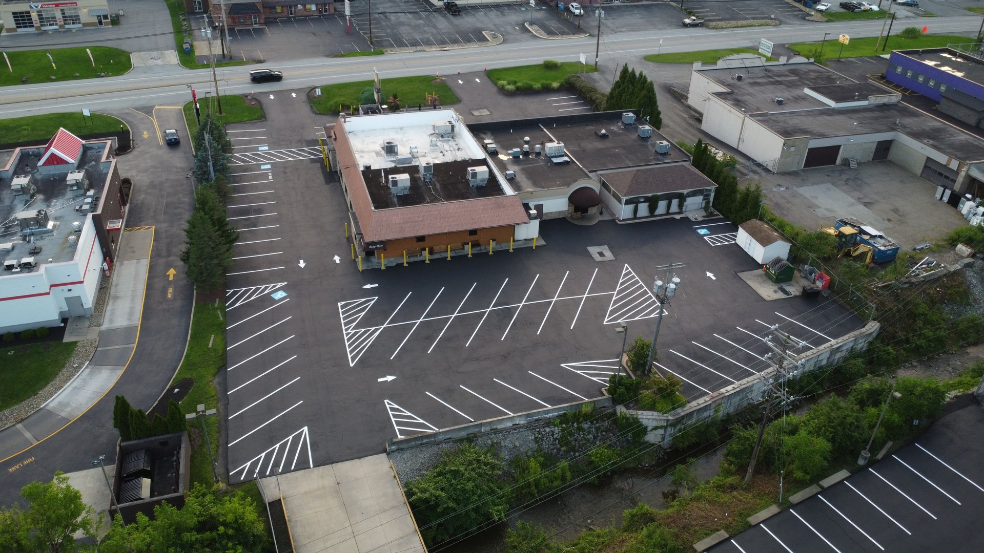 Aerial view of a small parking lot beside buildings, with white diagonal markings and a few parked cars.
