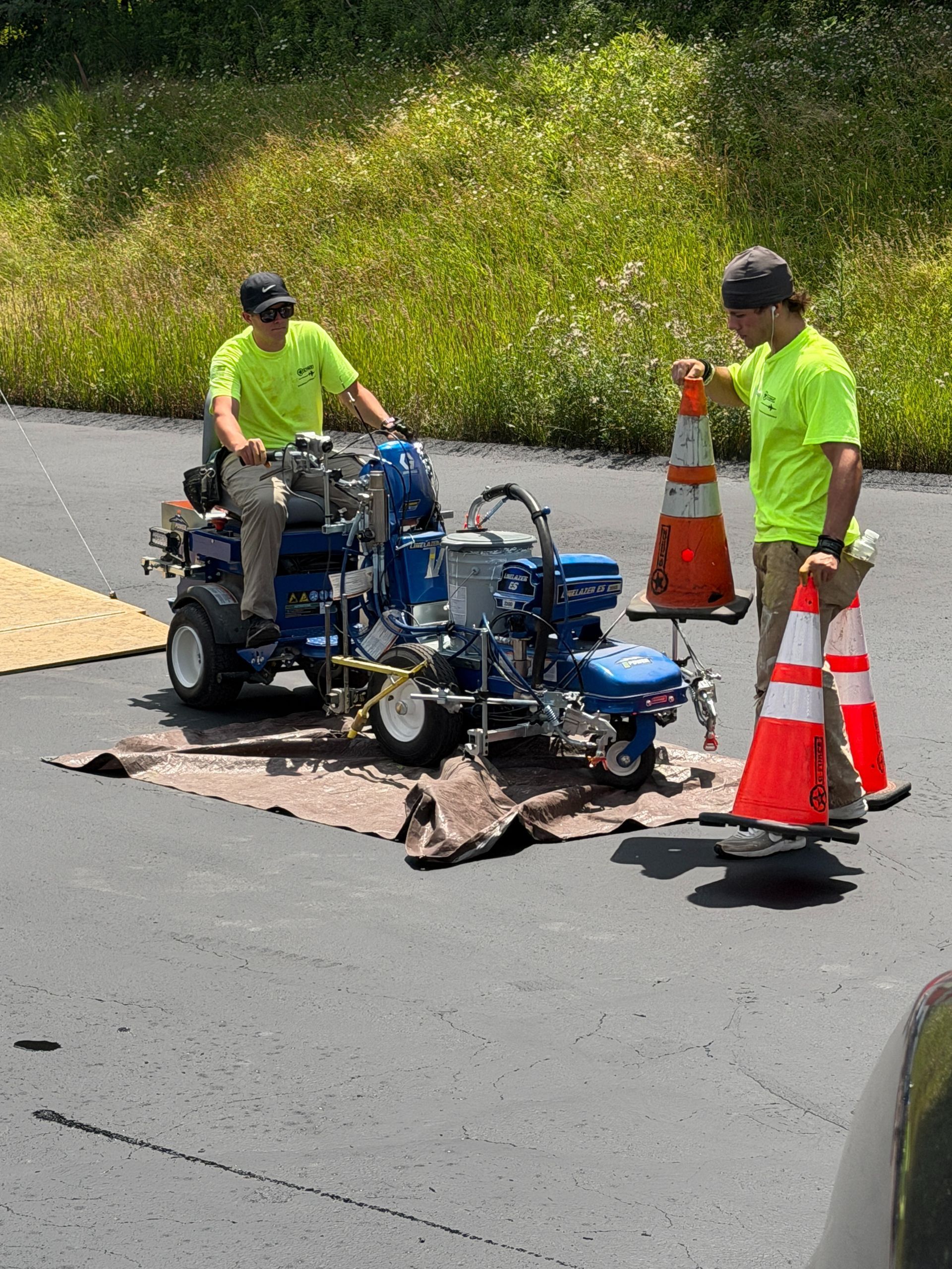 Workers inspecting a blue utility vehicle on the road beside orange traffic cones and a damaged patch of pavement