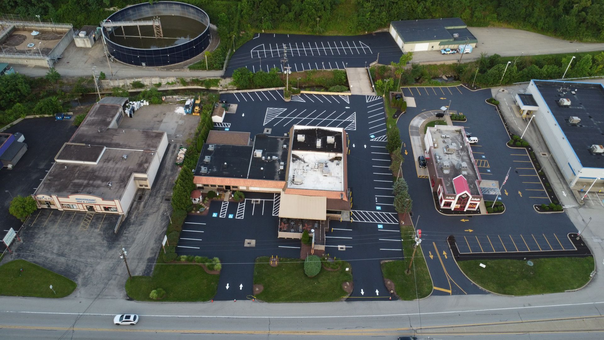 Aerial view of a commercial building, parking lots, and surrounding roads with multiple vehicles.