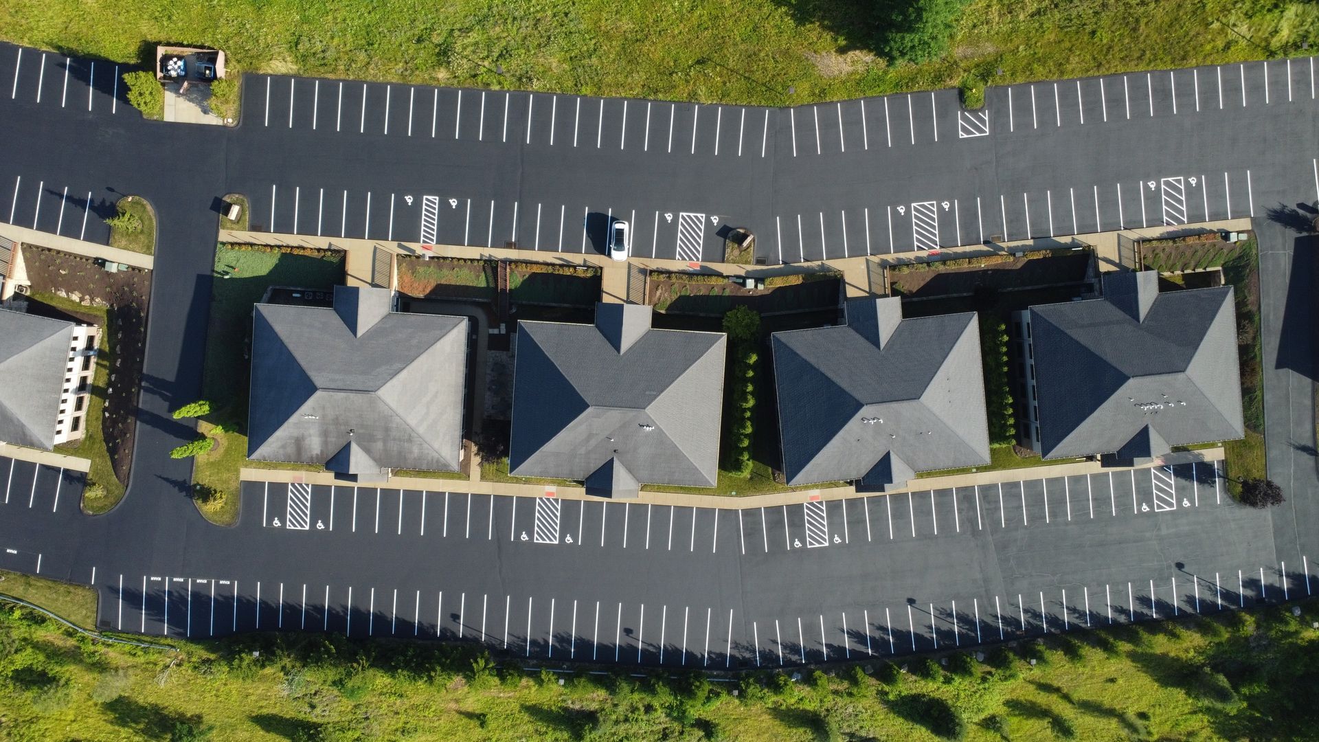 Aerial view of a row of gray-roofed townhouses with parking lots and green lawns.