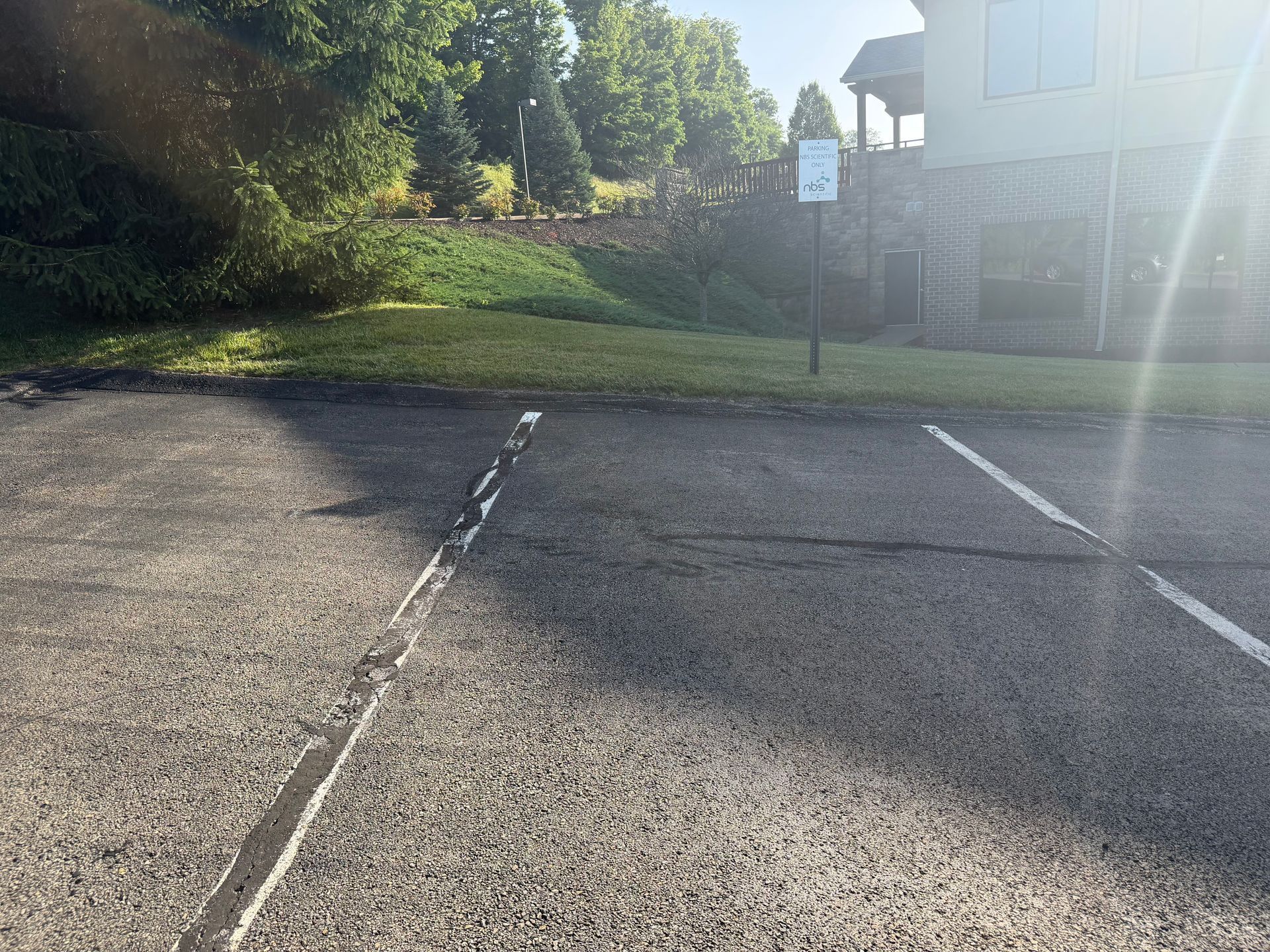 Empty asphalt parking lot beside a grassy slope and building in bright sunlight