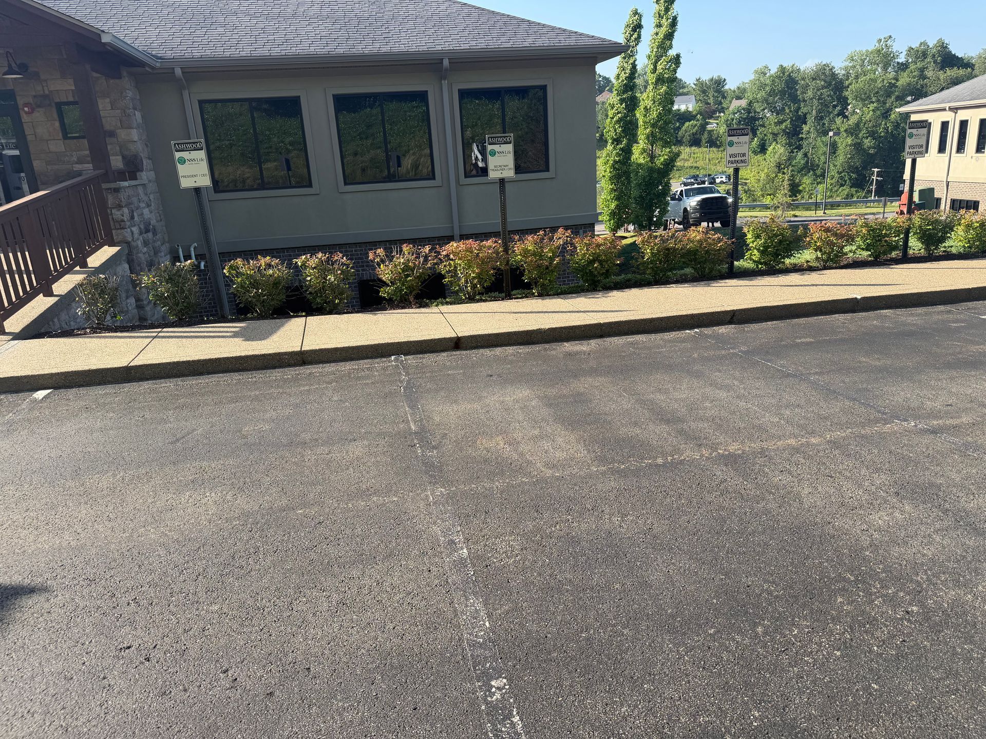 Brick office building with dark windows beside a paved parking lot and landscaped shrubs