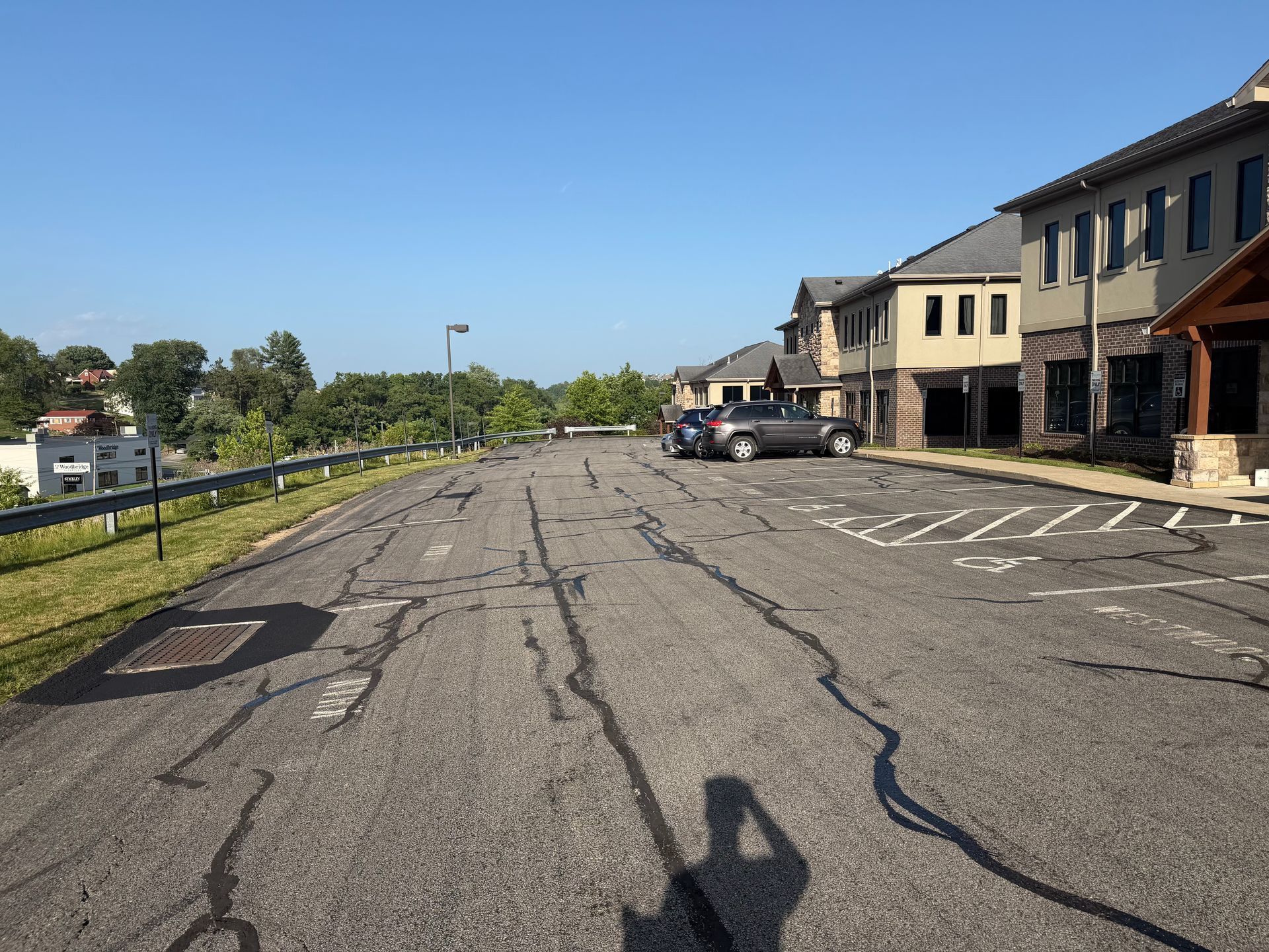 Empty parking lot beside row of townhouses on a sunny day, with cracked pavement and parked cars.