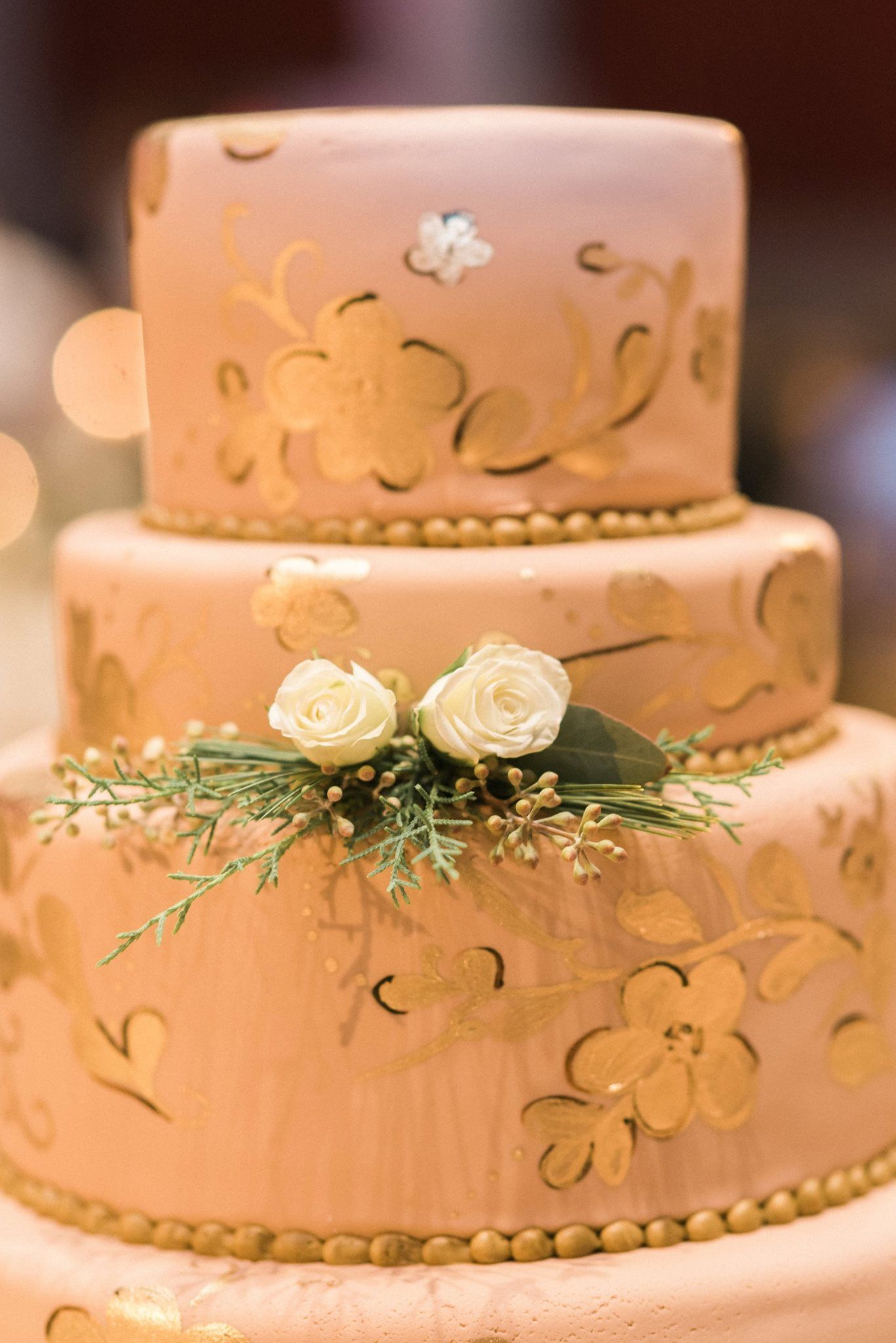 A close up of a three tiered wedding cake with flowers on top.