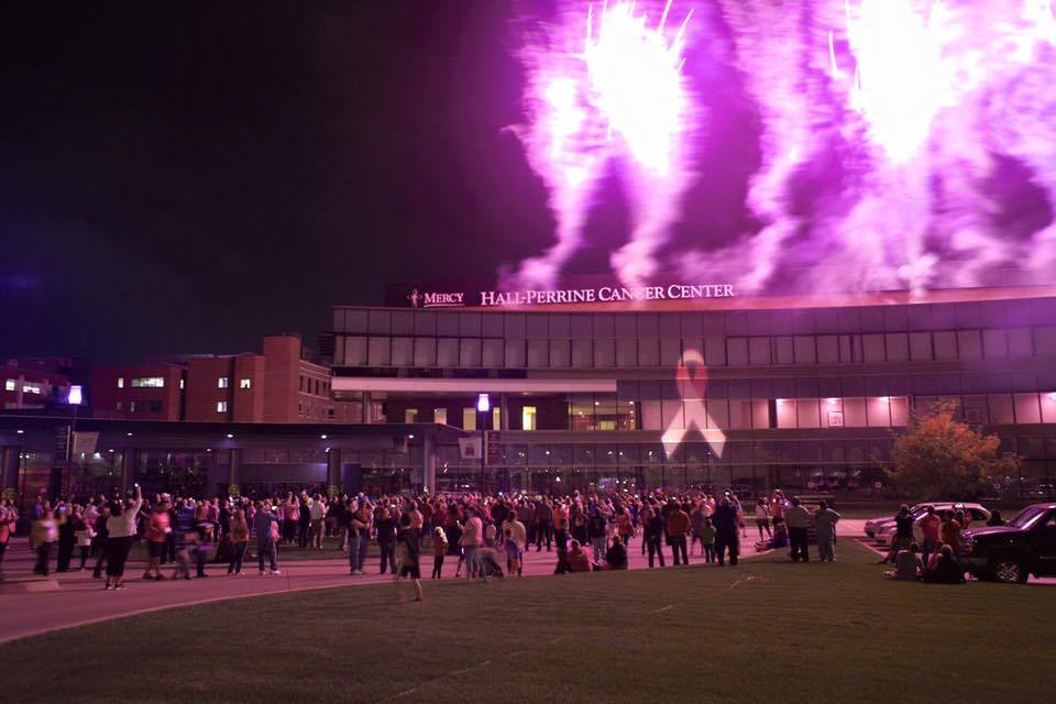 A crowd of people are watching a fireworks display in front of a large building.