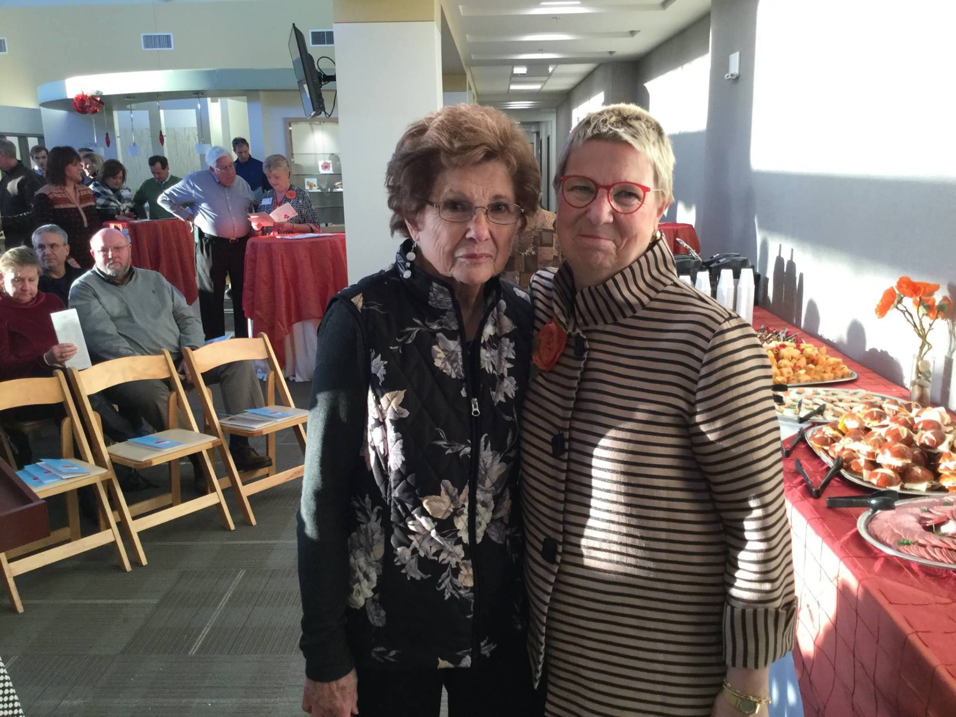 Two women are posing for a picture in front of a buffet table