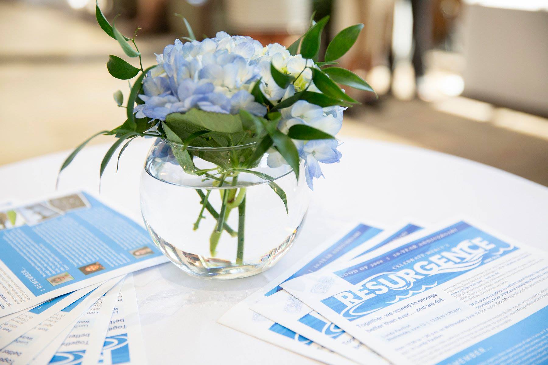 A vase of flowers is sitting on a table next to a stack of pamphlets.