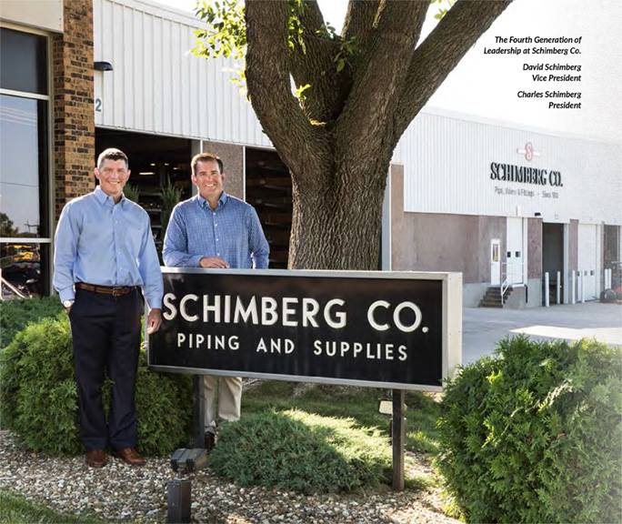 Two men standing in front of a sign that says schimberg co. piping and supplies
