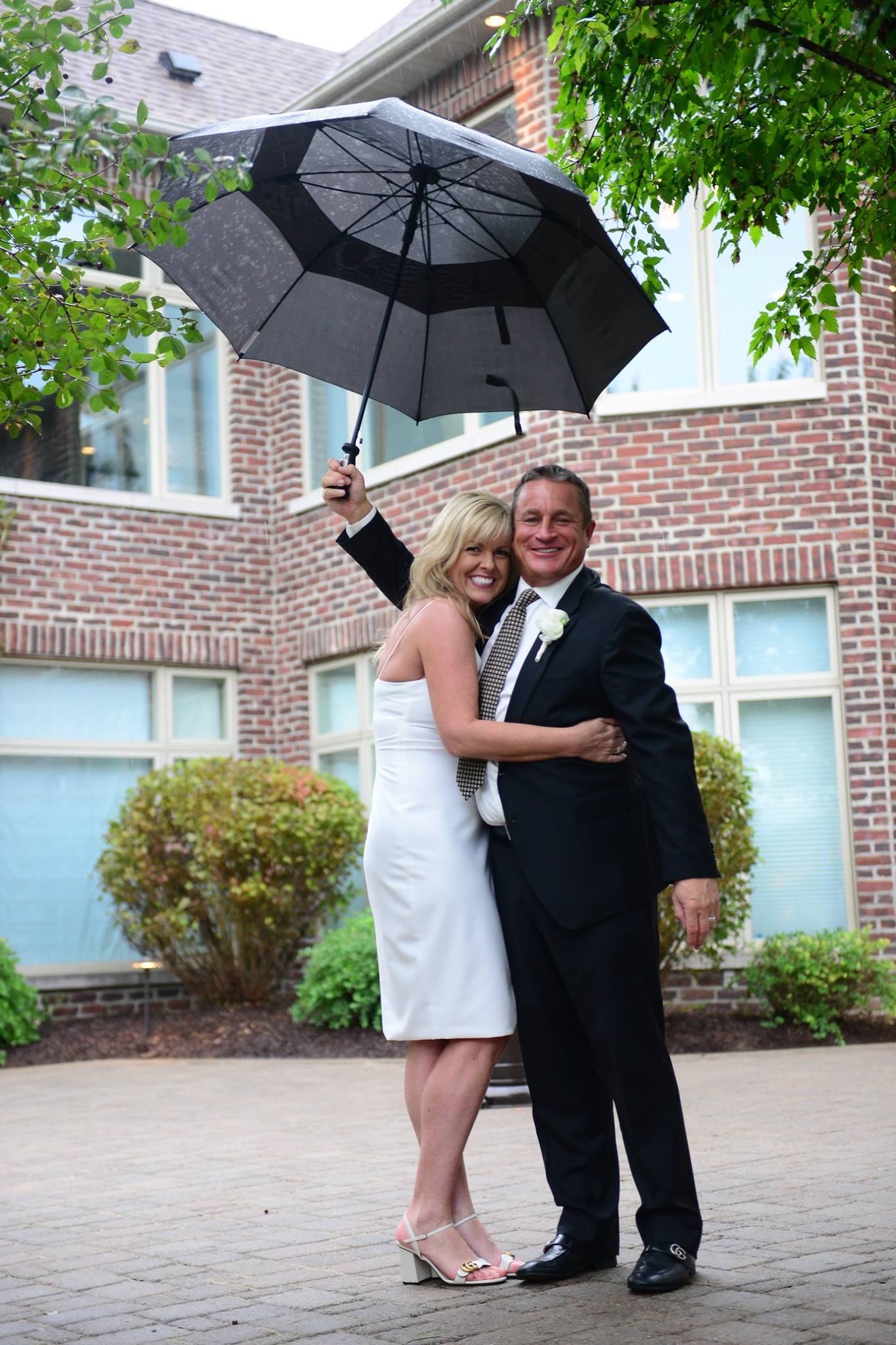 A bride and groom pose under an umbrella in front of a brick building