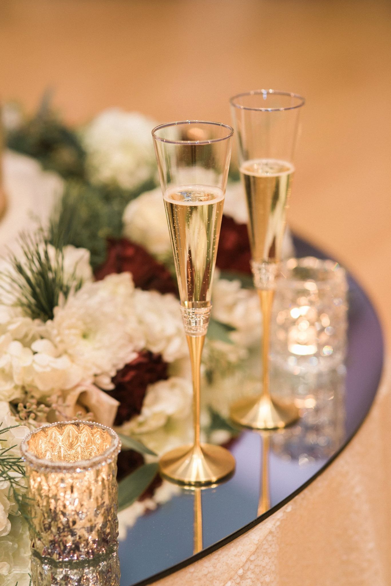 Two champagne flutes are sitting on a table with candles and flowers.