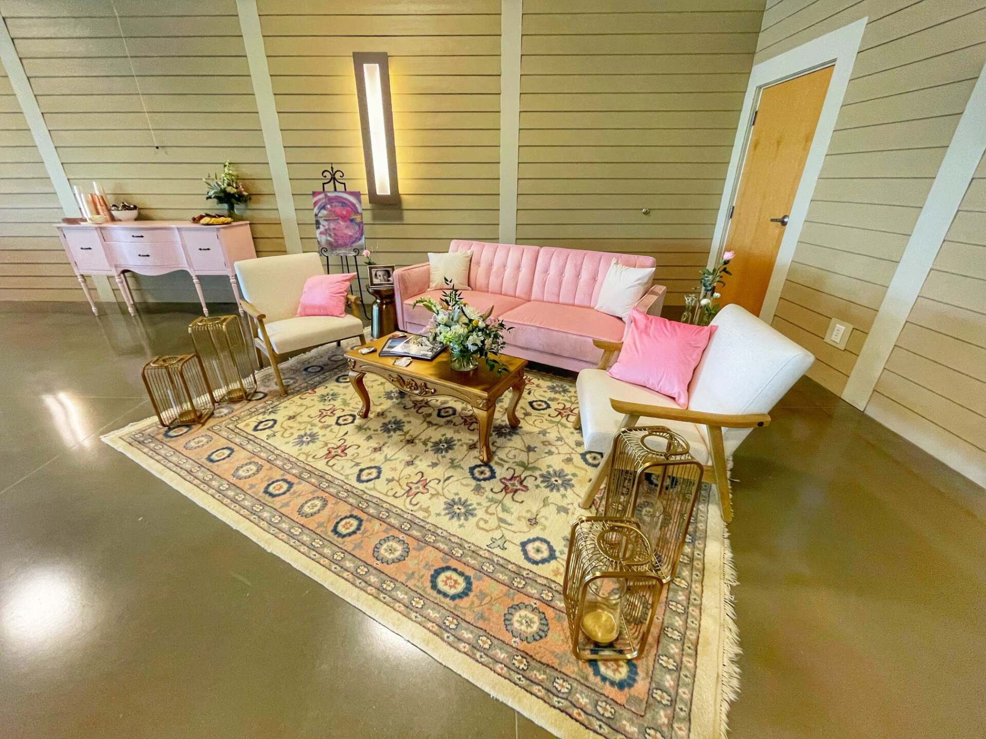 A living room with a pink couch , chairs , and a rug.