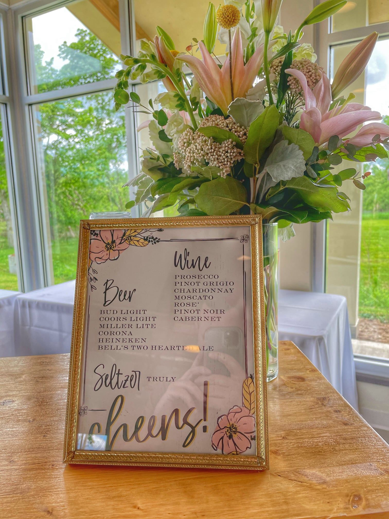 A framed menu is sitting on a wooden table next to a vase of flowers.