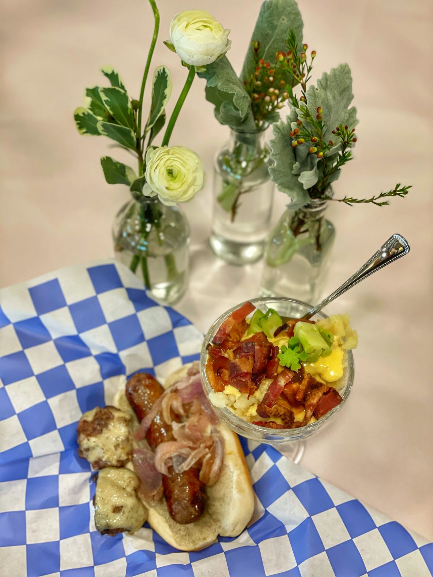 A hot dog and a bowl of food are on a checkered table cloth.